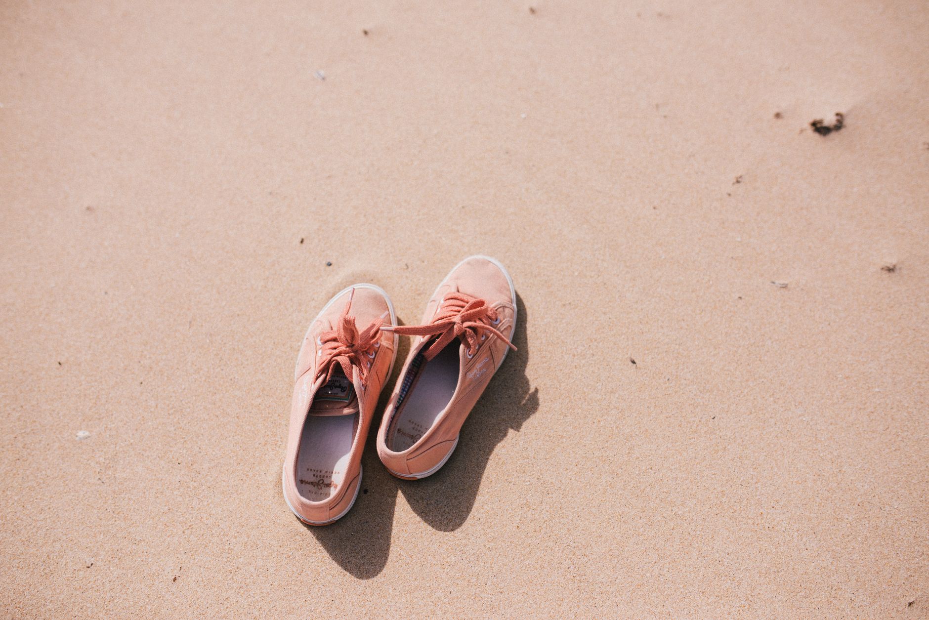 Pair of pink sneakers left on a sandy beach in bright sunlight, conveying a summer vibe.