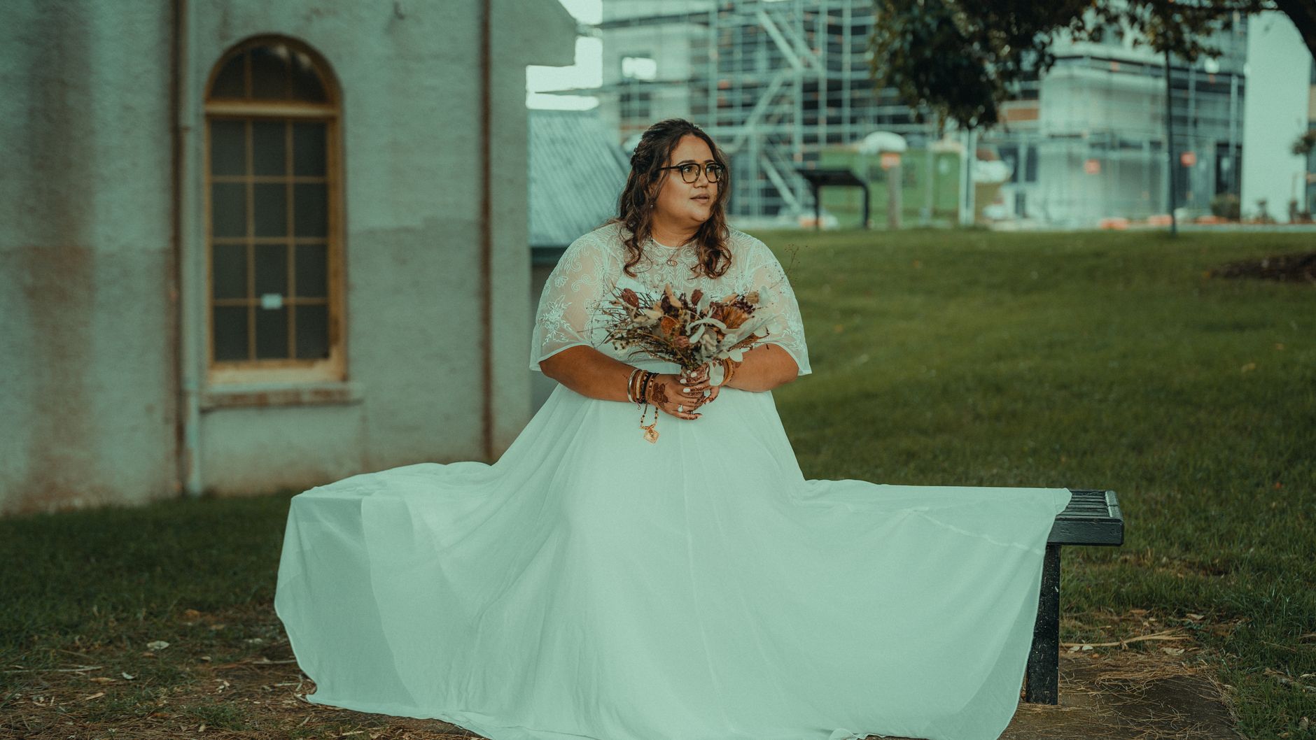 Plus-size bride in wedding dress holding bouquet, elegantly posing outdoors.