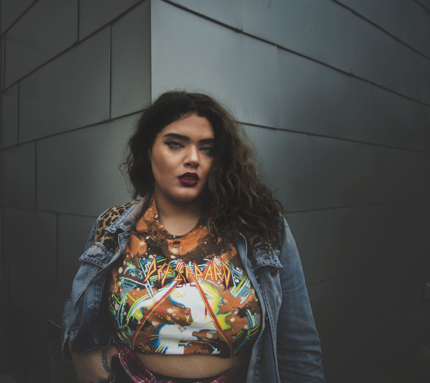 Confident young woman in fashionable attire posing outdoors against a sleek urban wall.