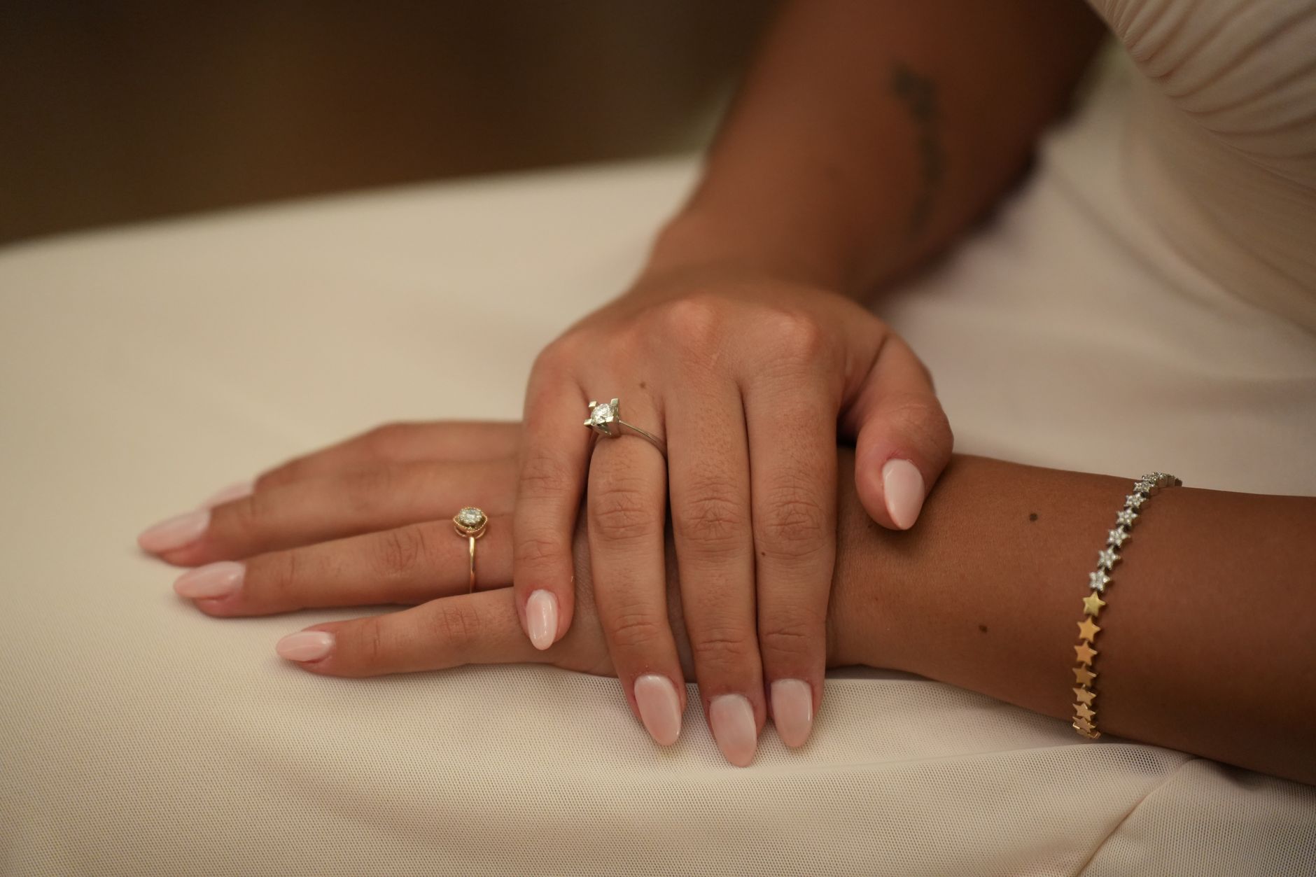 A close-up photo showcasing elegant manicured hands adorned with rings and a bracelet.