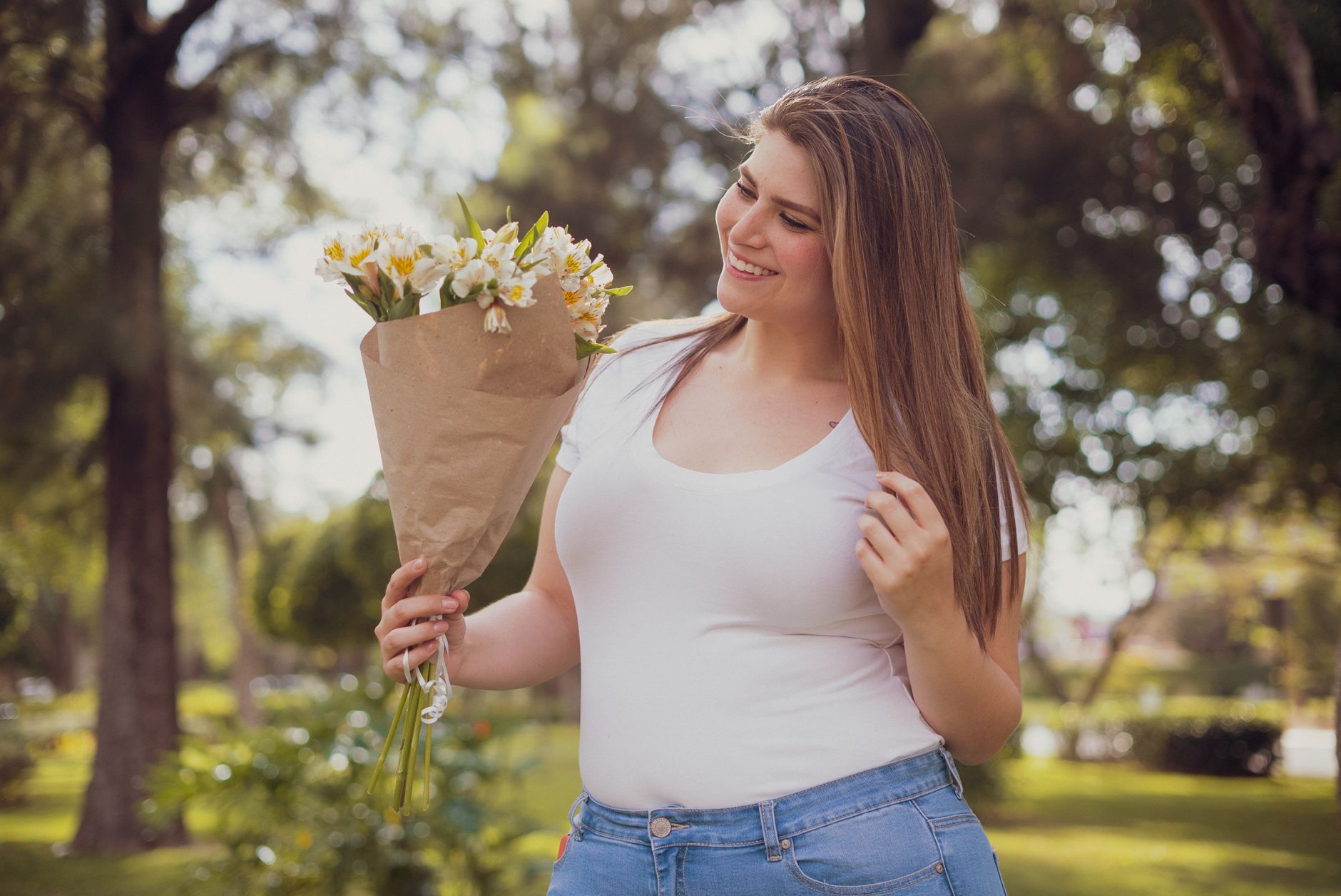 A cheerful woman holding a bouquet of flowers enjoys a sunny day in the park.