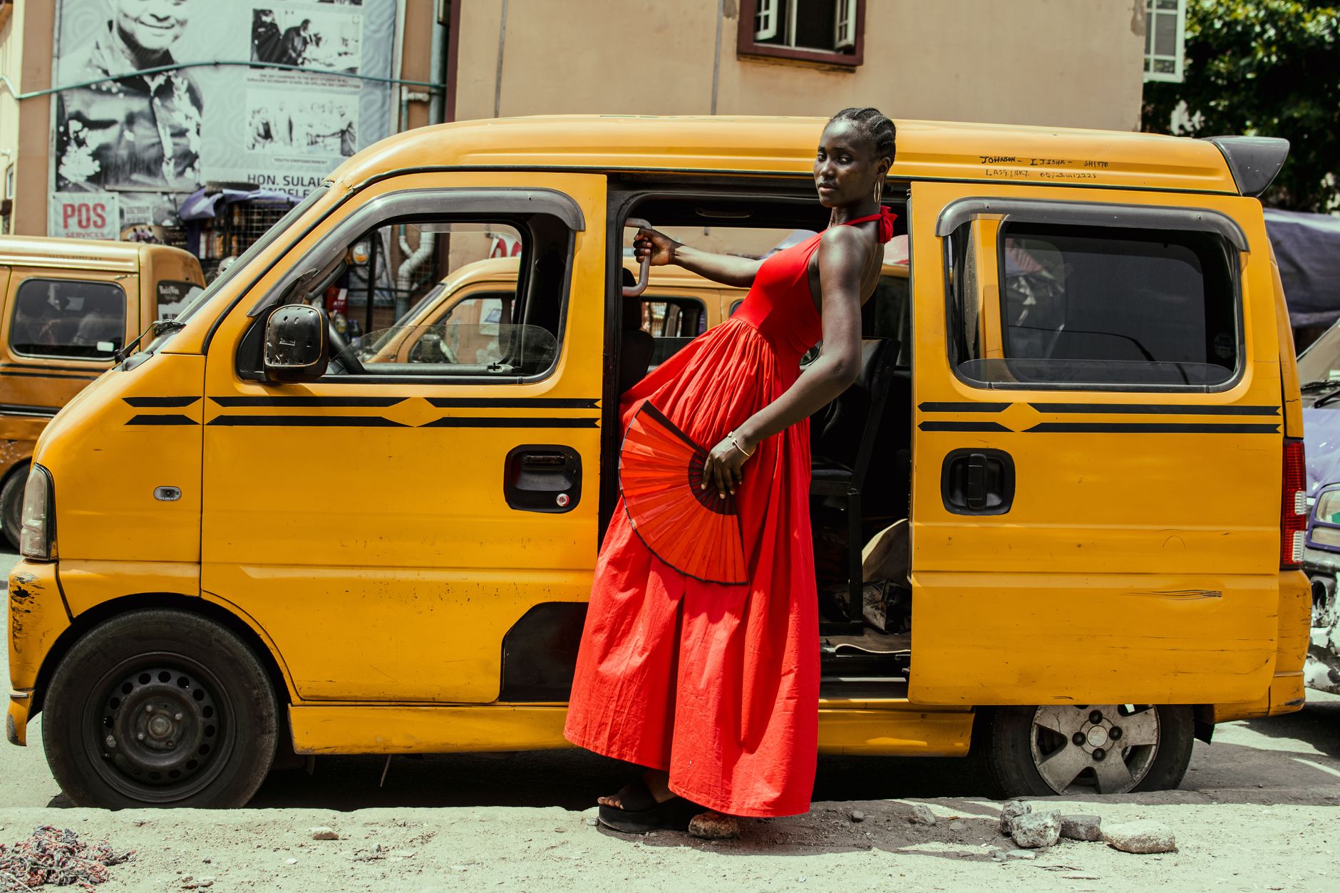 Fashionable woman in a red dress posing confidently beside a yellow bus.