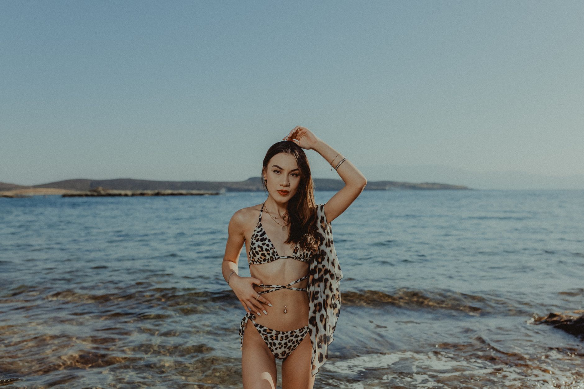 A young woman in a bikini stands by the sea on a sunny summer day, enjoying the warm beach environment.