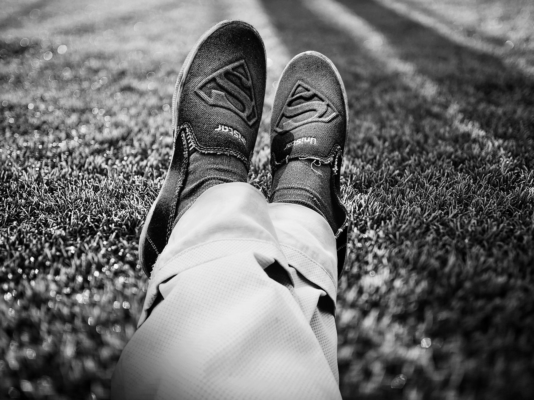 Black and white image of person wearing sneakers, relaxing on grass.
