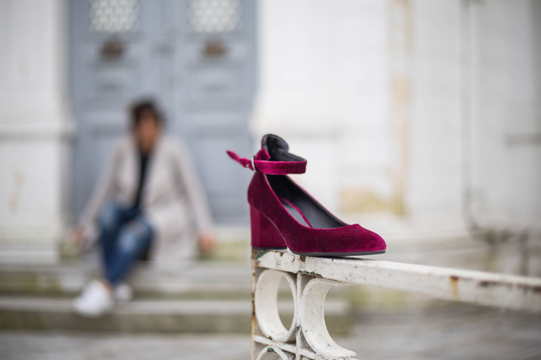 A stylish burgundy high heel on a vintage railing, with blurred outdoor background.