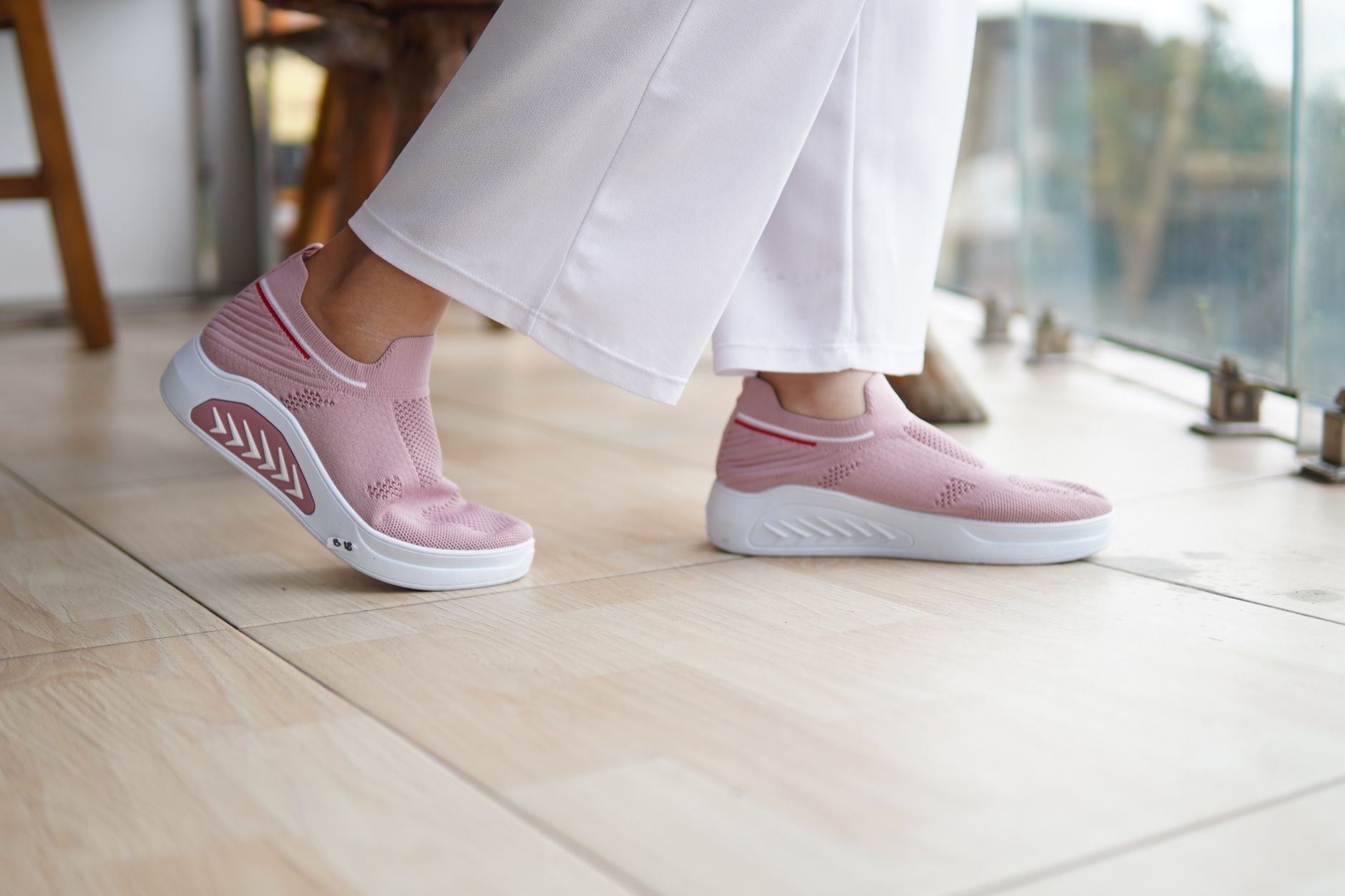 Close-up of pink knit slip-on sneakers paired with white pants, suitable for casual fashion.