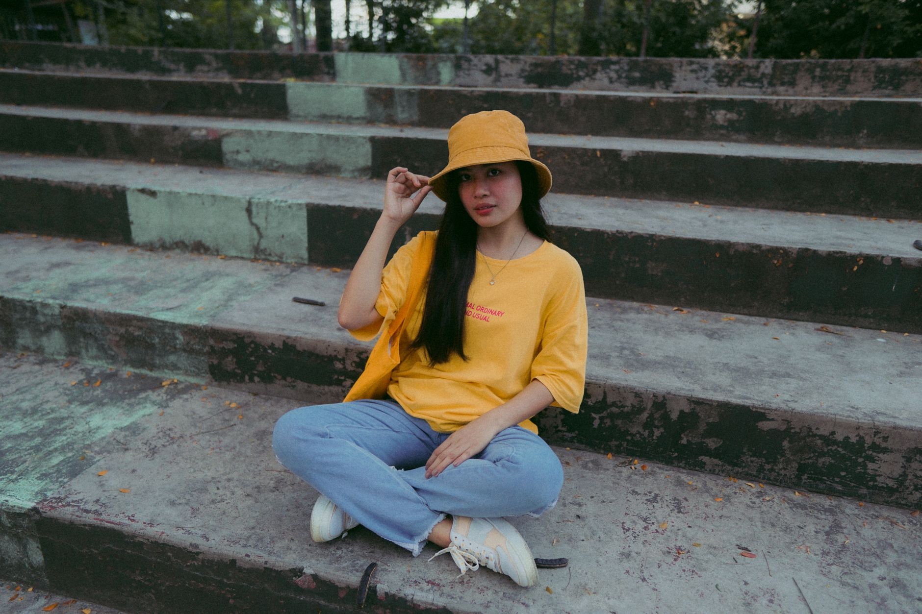 Fashion-forward woman in a bucket hat and casual attire sitting on outdoor stairs, exuding style and confidence.