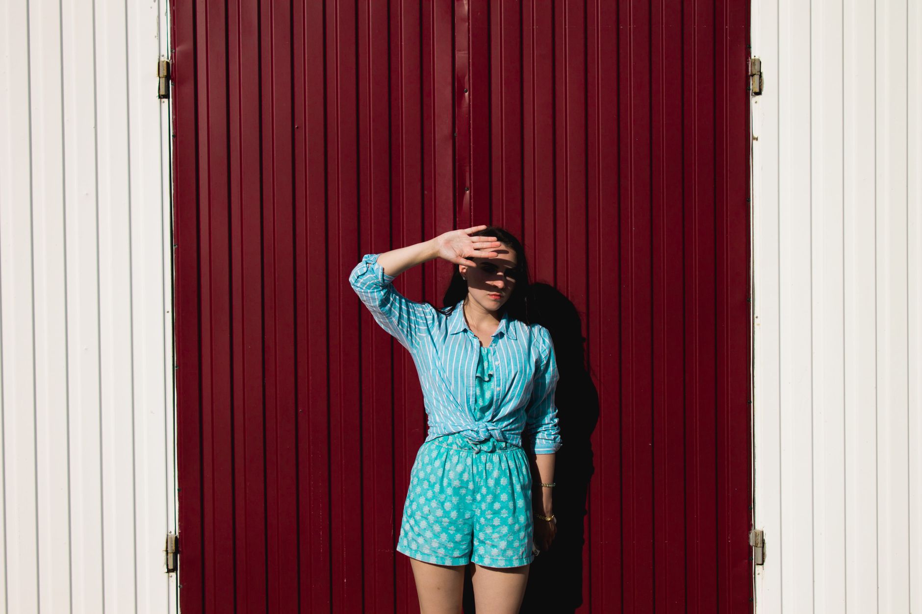 Fashionable woman with hand over face against vintage red door background outdoors.