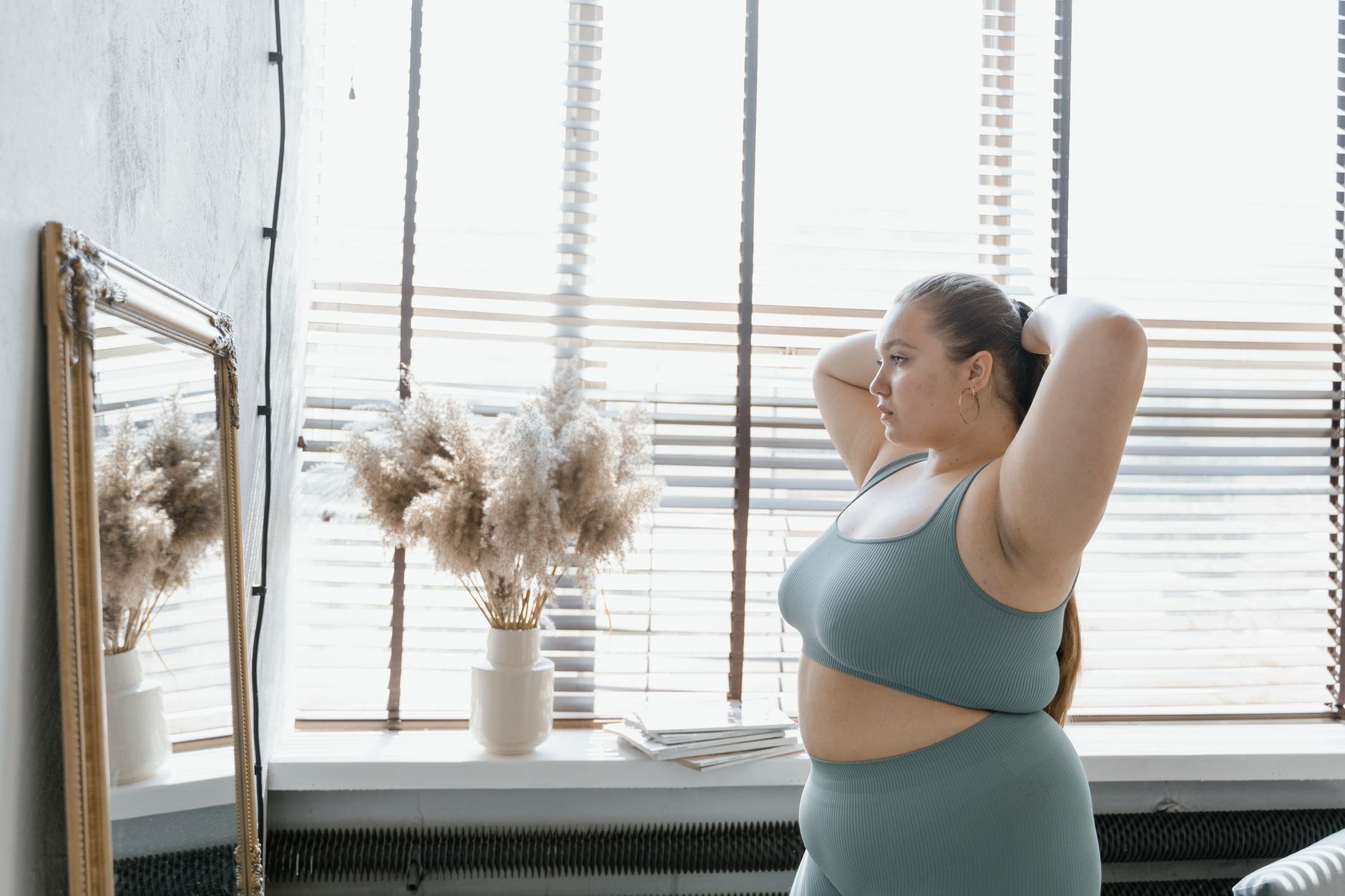 A plus-size woman in activewear admires her reflection indoors, promoting body positivity and self-esteem.