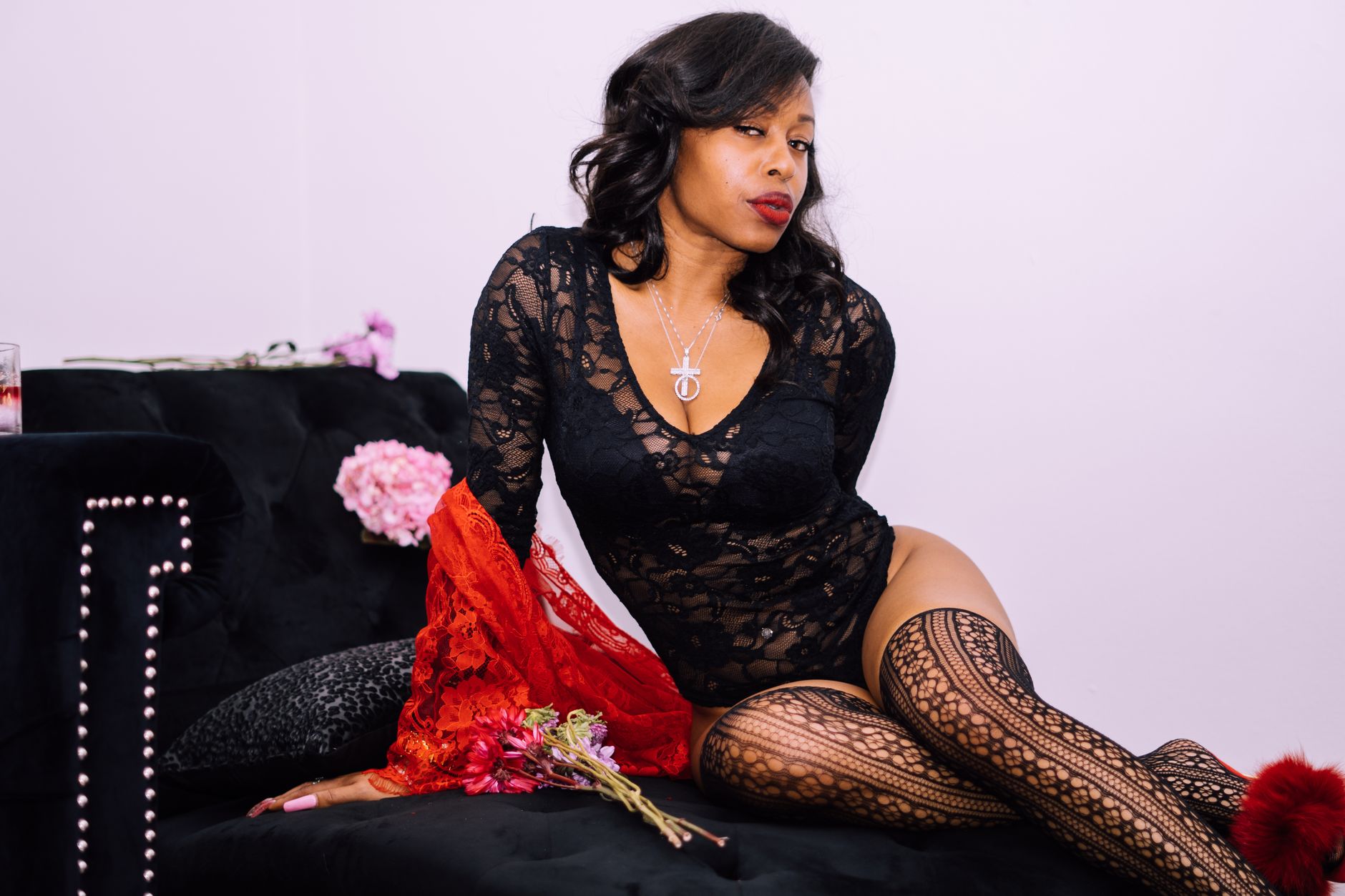 Stylish woman in lace lingerie sitting with a confident pose on a black sofa.