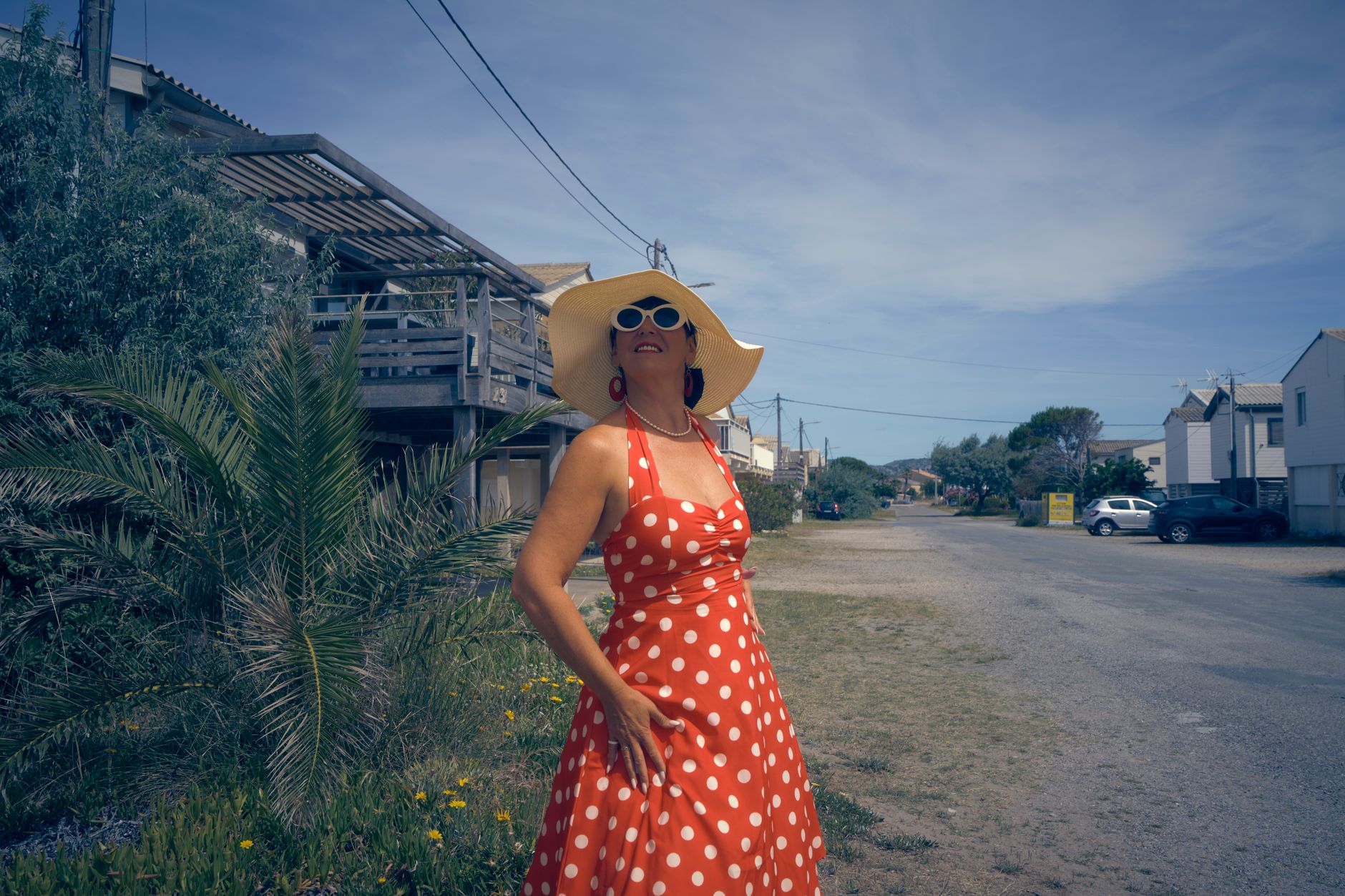 Stylish woman in a red polka dot dress with a sun hat enjoys a sunny day outdoors, capturing retro vibe.