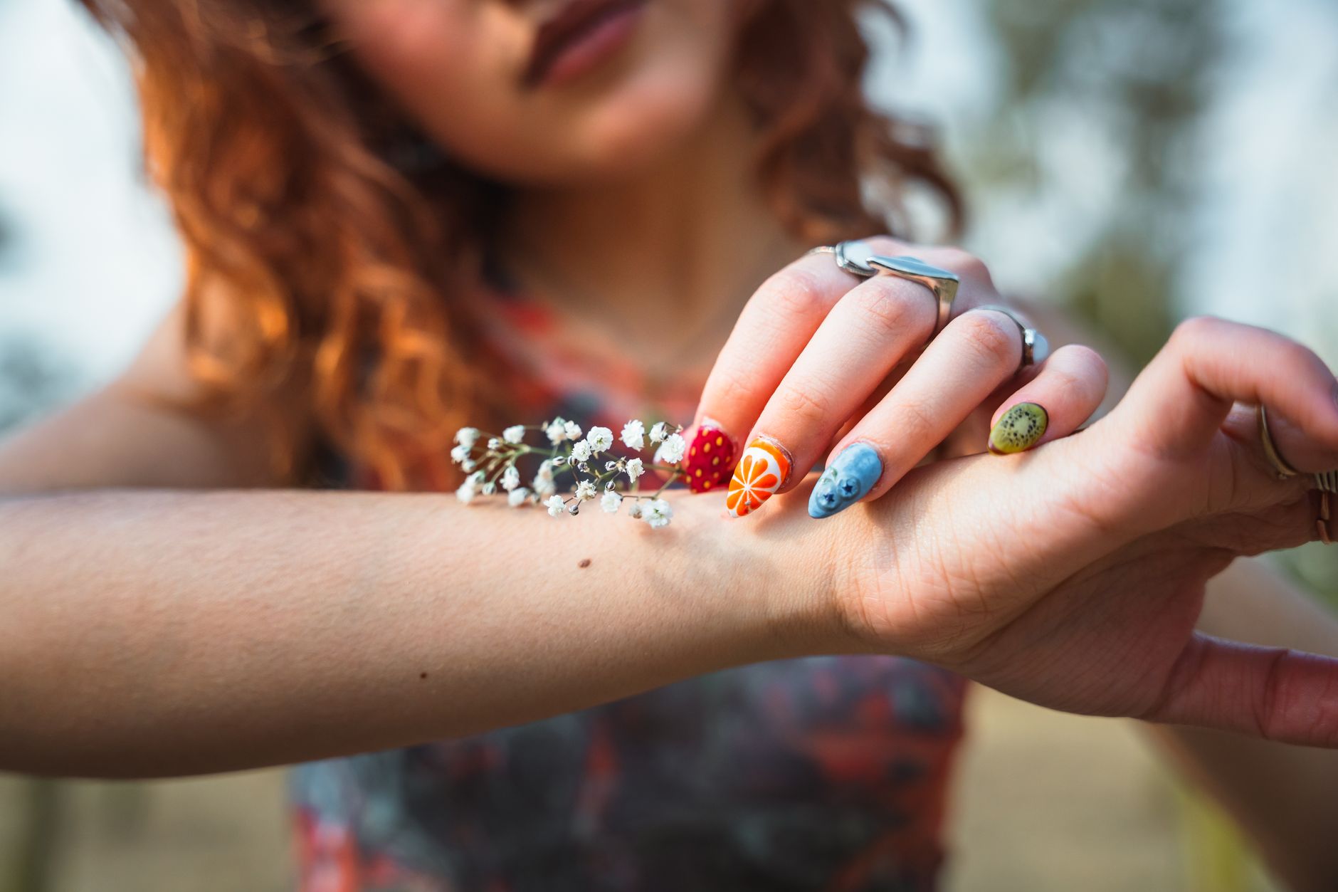 Close-up of a woman's hand showcasing vibrant and artistic nail art designs outdoors.