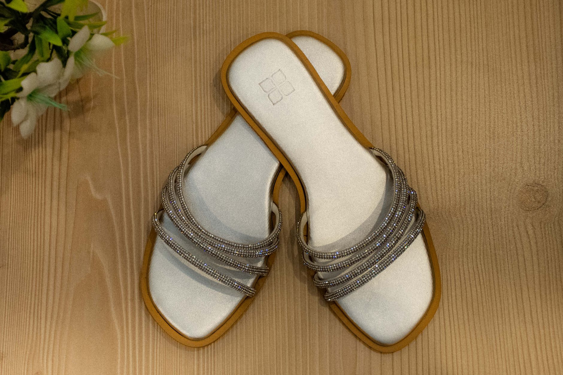 Pair of stylish silver sandals with decorative beads showcased on a wooden floor, perfect for casual wear.