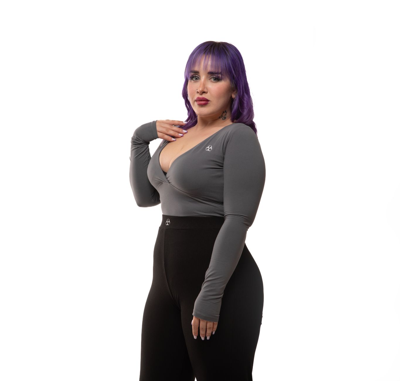 A confident woman in gray sports top and black leggings posing in studio.