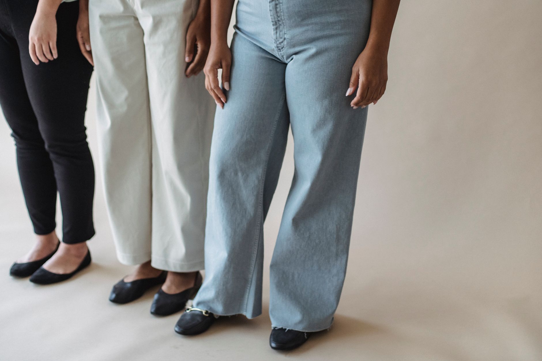Three women standing in stylish pants showcasing diverse fashion on a neutral background.