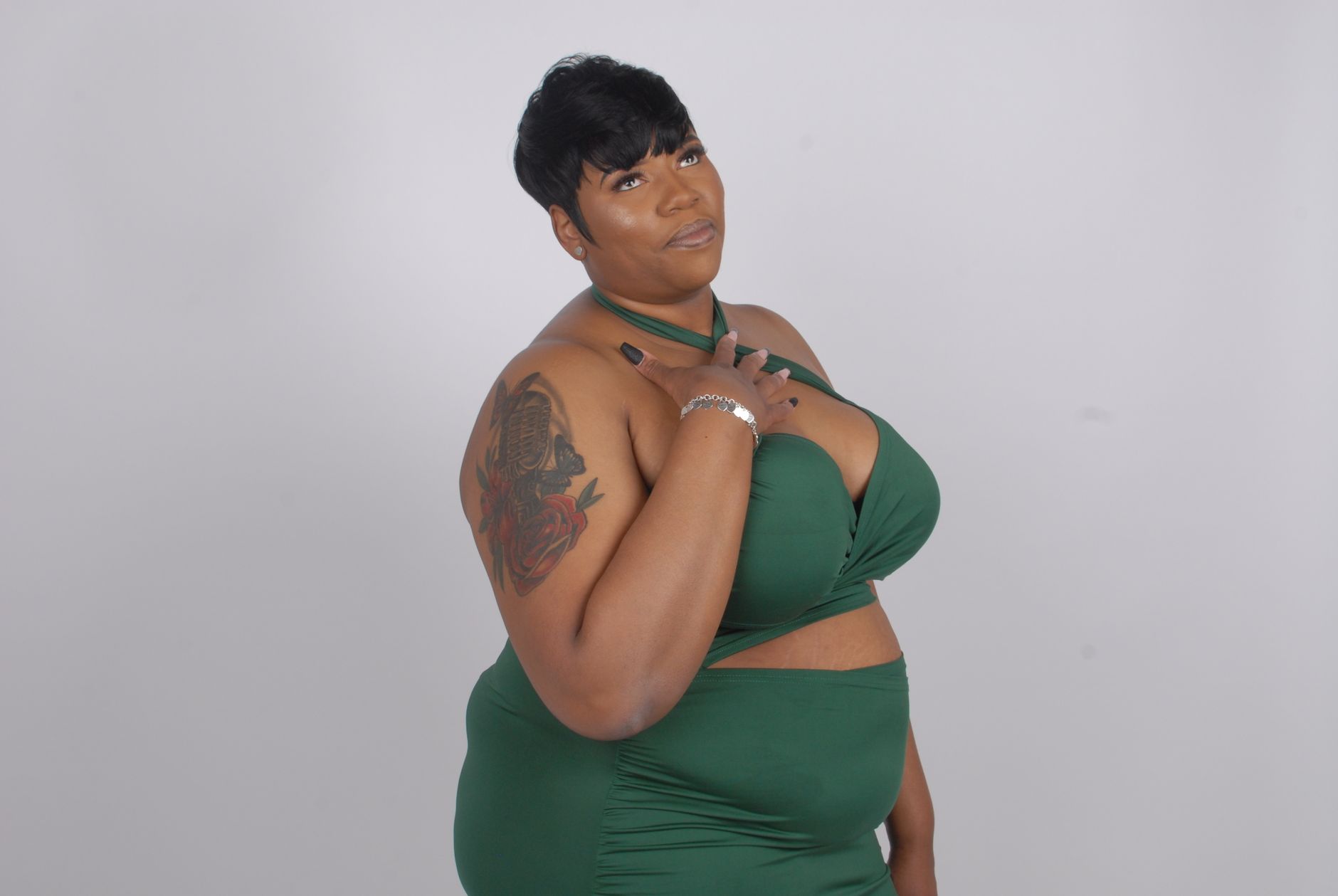 Elegant plus-size woman posing confidently in green attire against a plain backdrop.