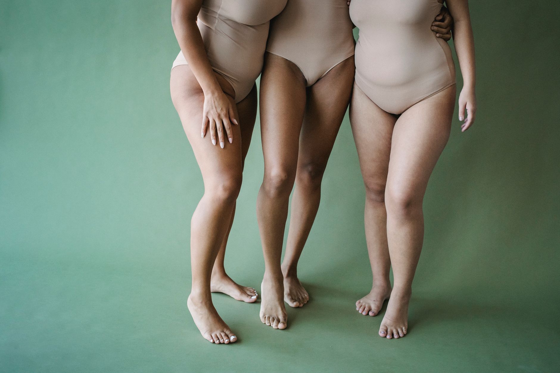 Three women in beige swimsuits showcasing body positivity and diversity on a green background.