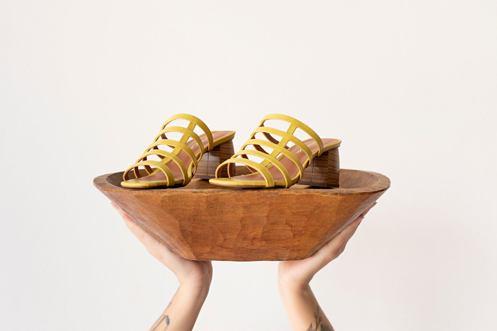 Modern yellow heeled sandals presented creatively on a wooden bowl.