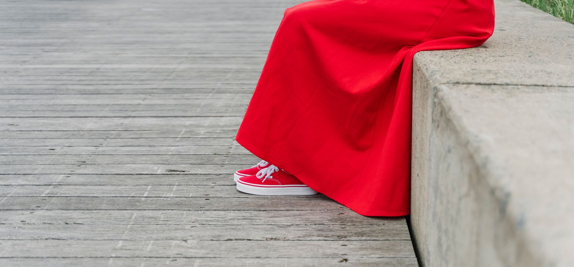 A person sitting on a concrete bench in a red dress with matching shoes.