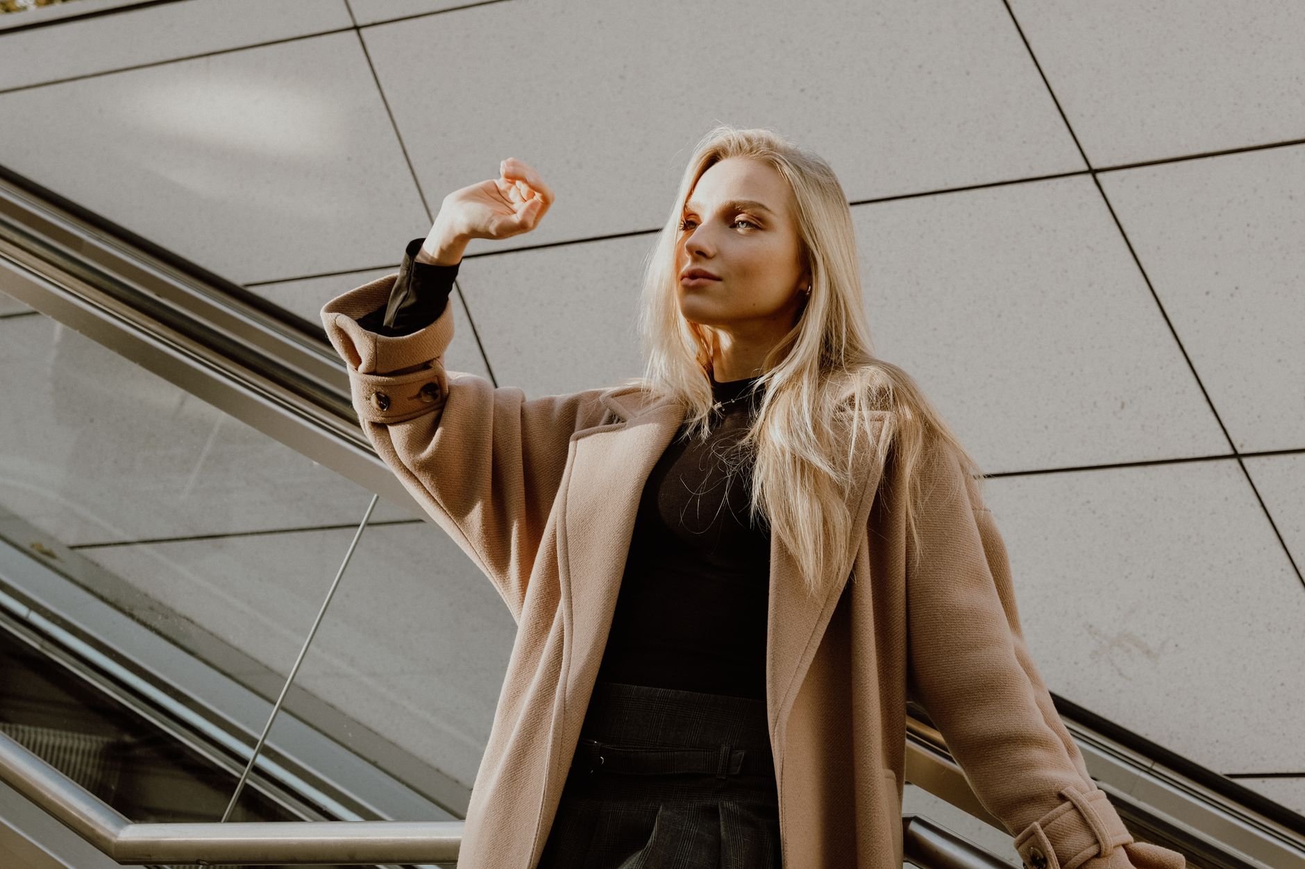 Blonde woman elegantly poses in a wool coat outdoors, exuding style and fashion.