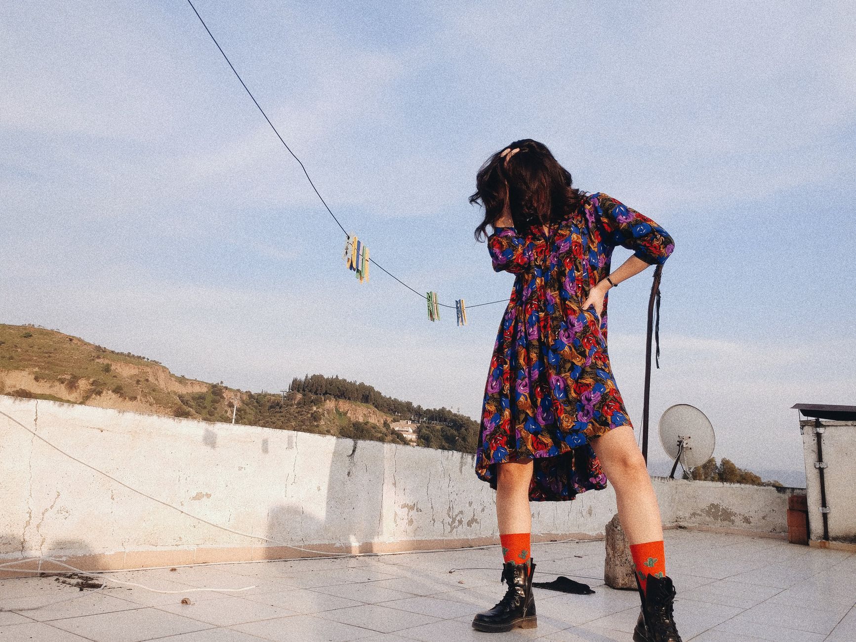 Stylish woman posing on a rooftop, wearing a vibrant dress with the city skyline in the background.