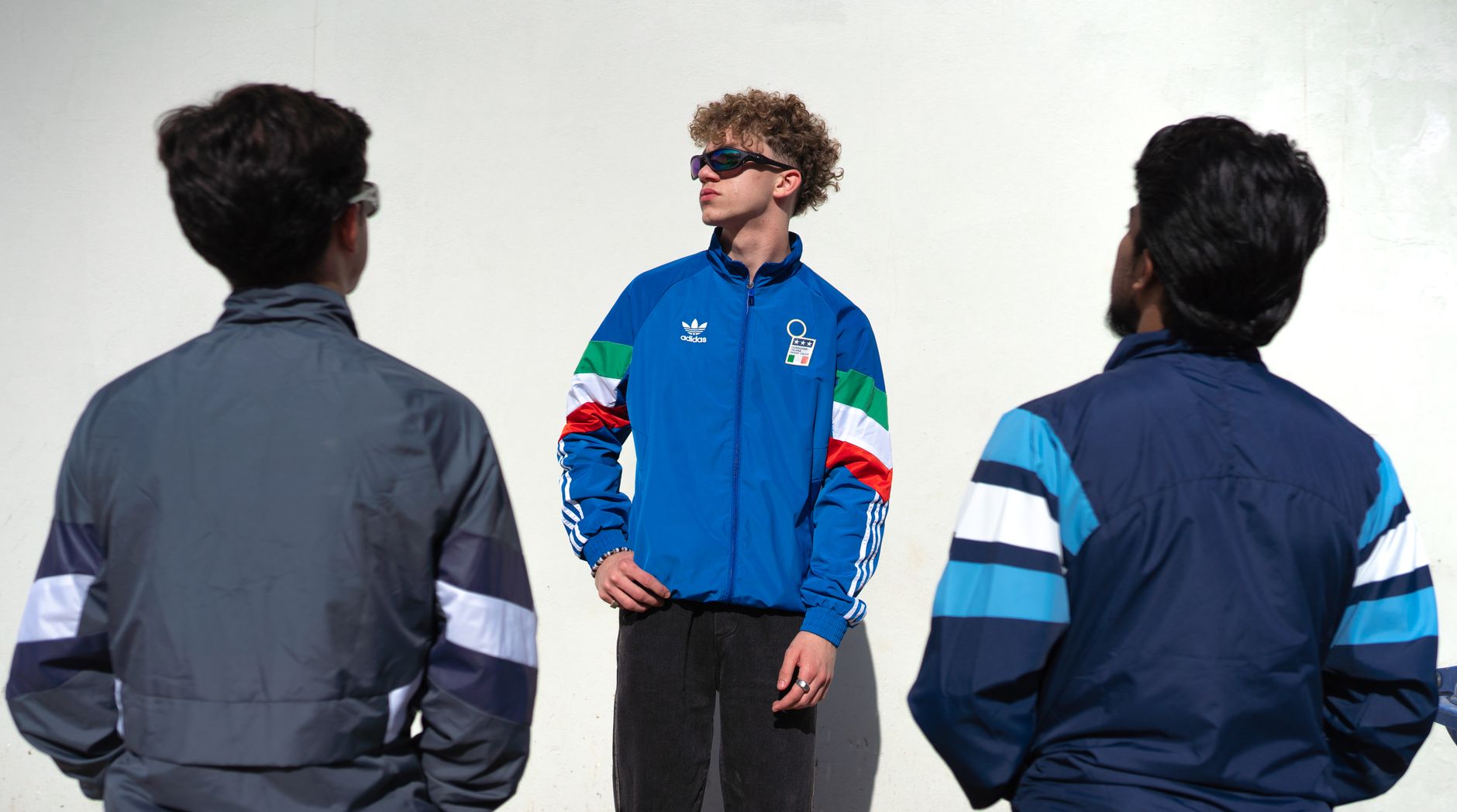 A group of young adults wearing colorful track jackets standing confidently outdoors.