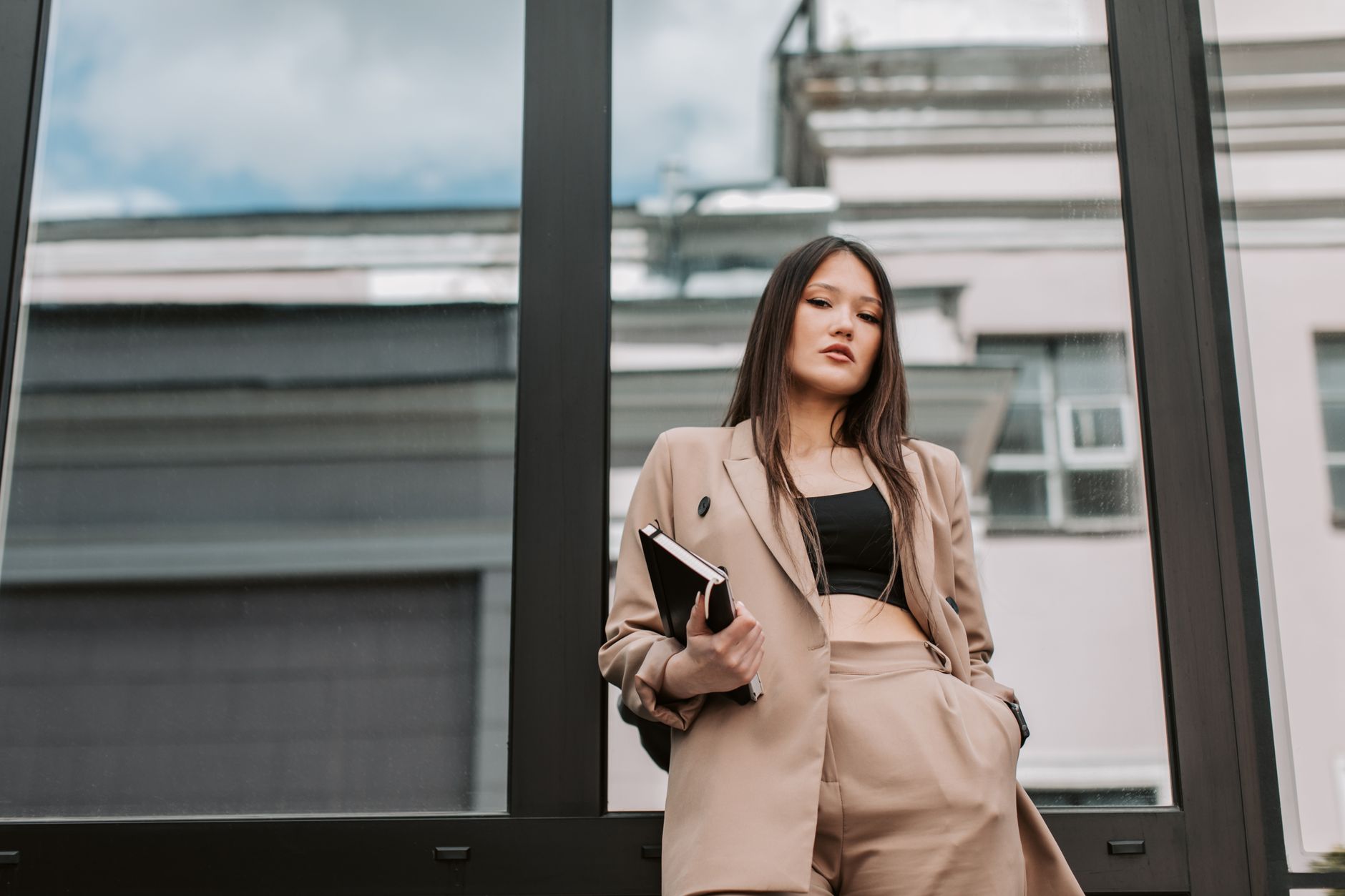 Stylish Asian woman in sharp corporate attire posing confidently against a glass wall.