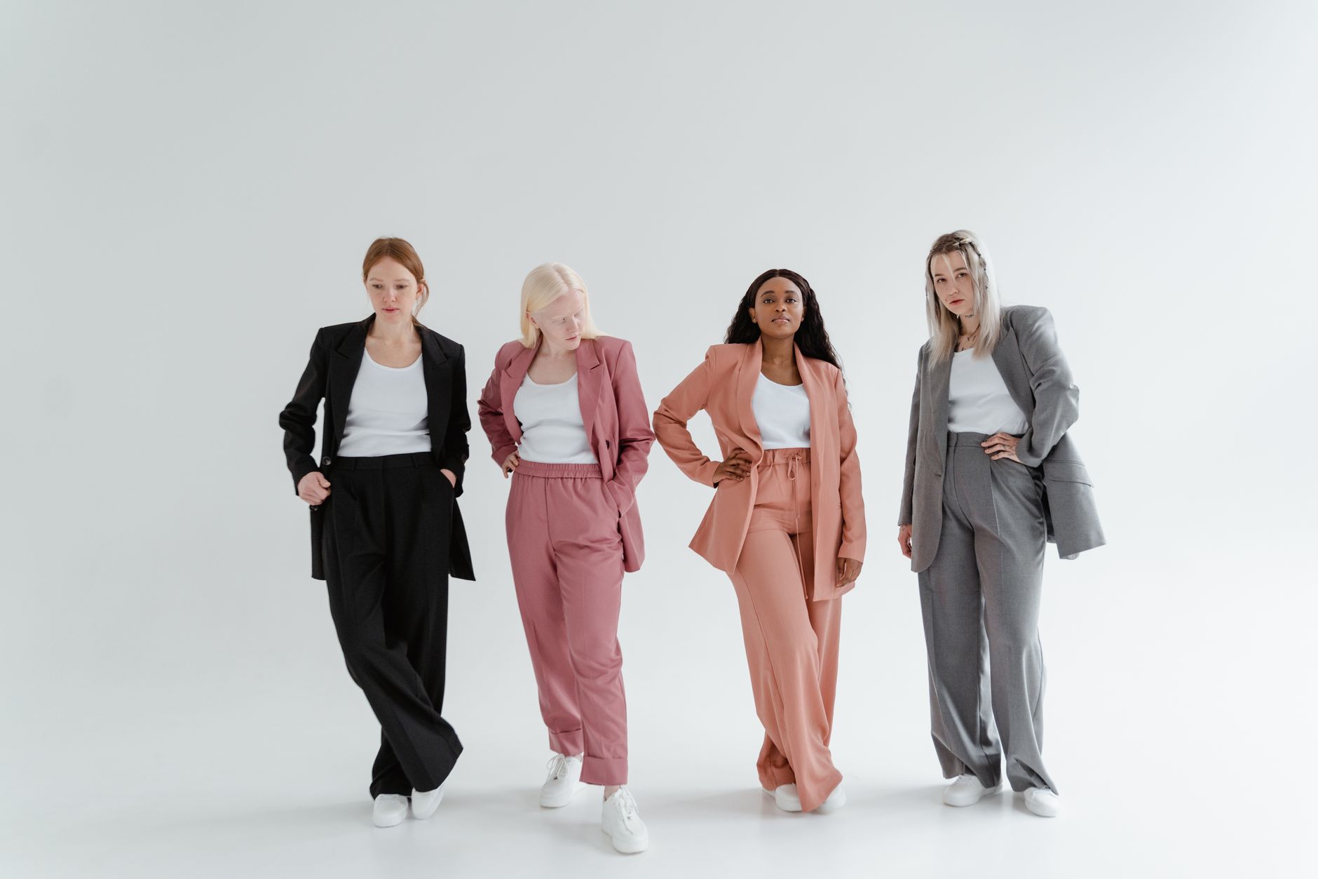 Four women posing confidently in colorful business suits against a white studio background.