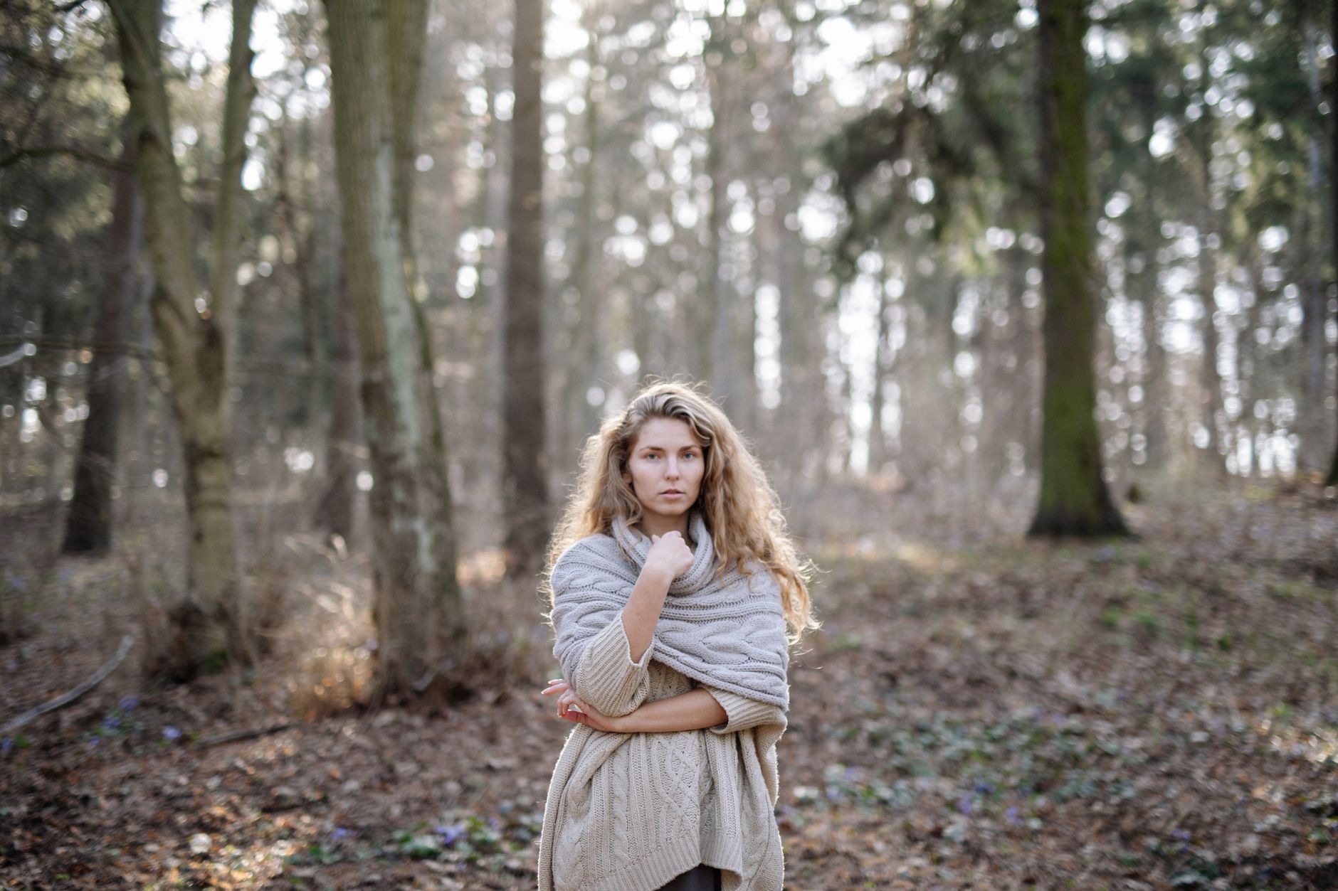 Young woman in a cozy sweater standing in a serene autumn forest.