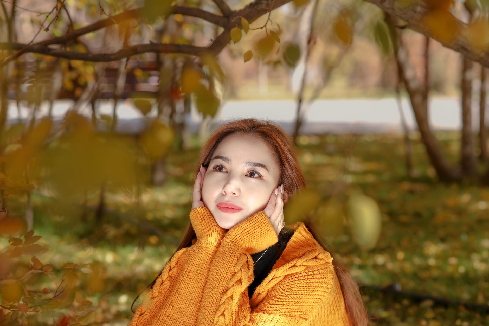 A woman in a cozy yellow sweater enjoys a serene autumn day outdoors under colorful foliage.