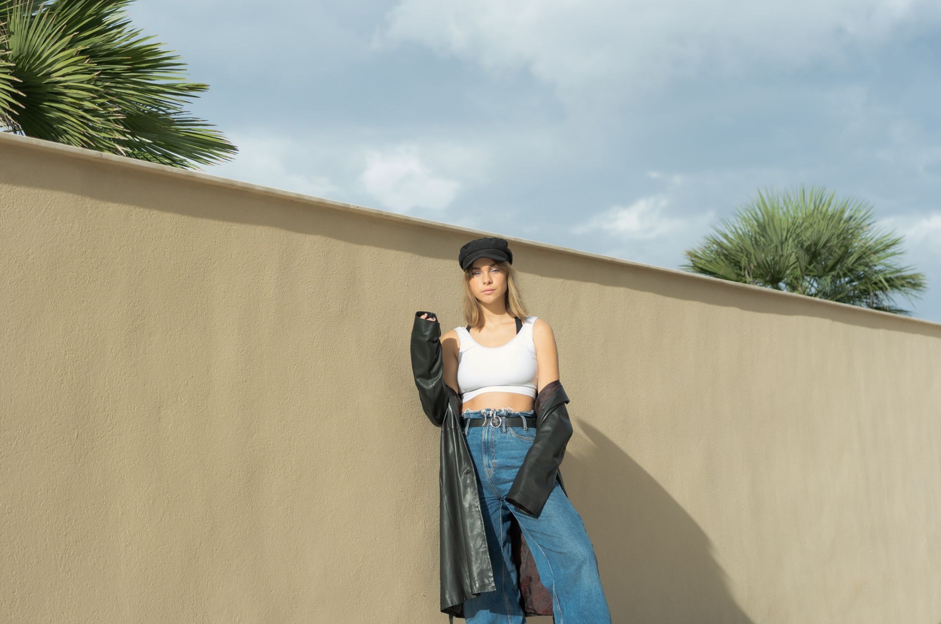 Stylish woman in 90s fashion standing by a wall under a sunny sky.