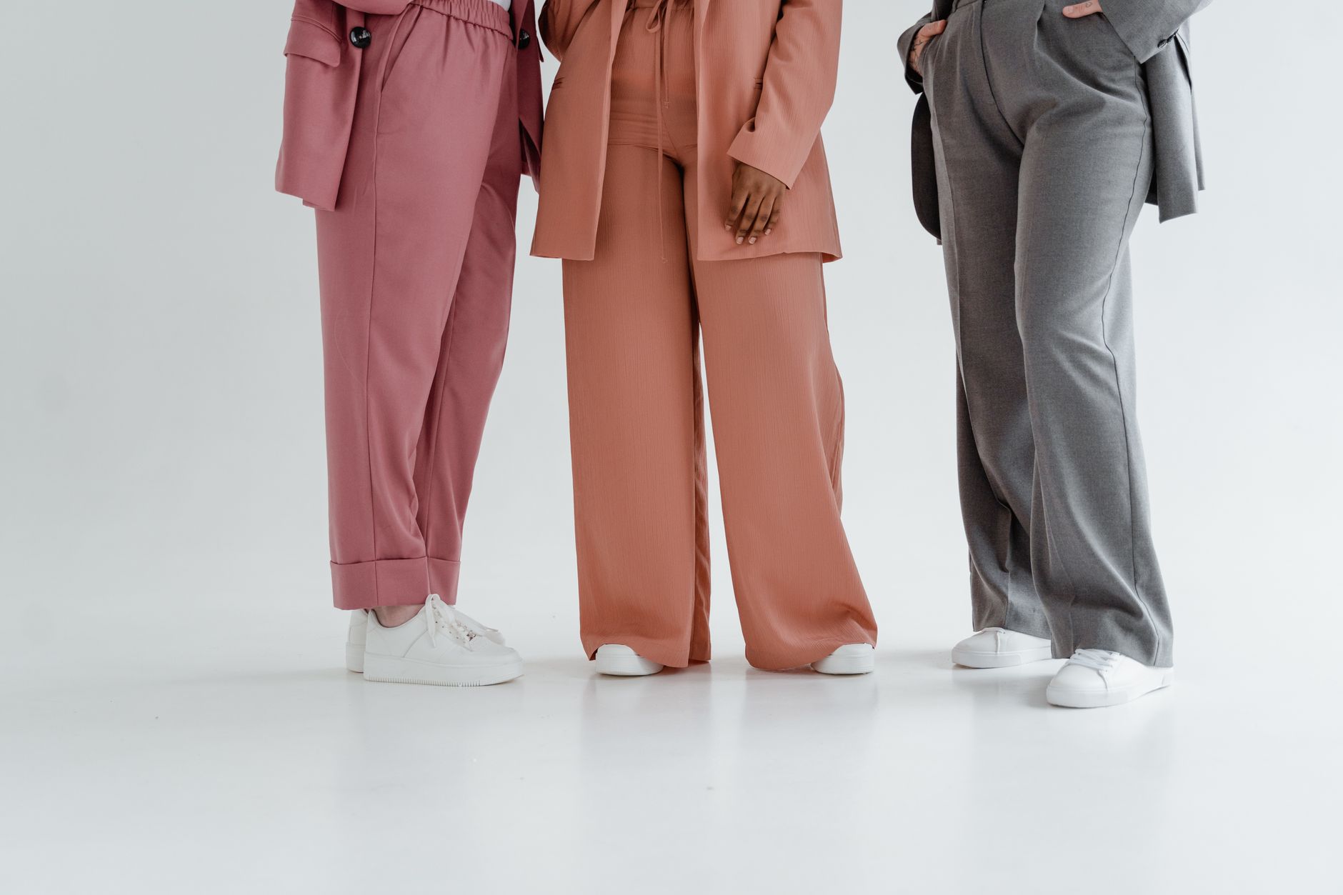 A stylish studio shot showcasing three colorful trouser styles with white sneakers on a clean background.