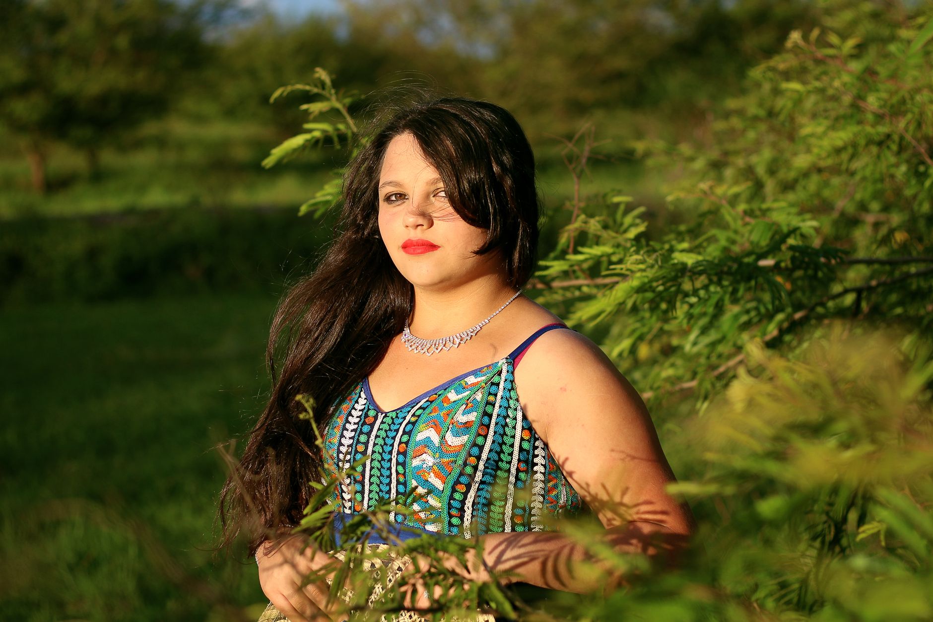 A plus-size woman with black hair and red lips poses outdoors in a vibrant, printed dress.