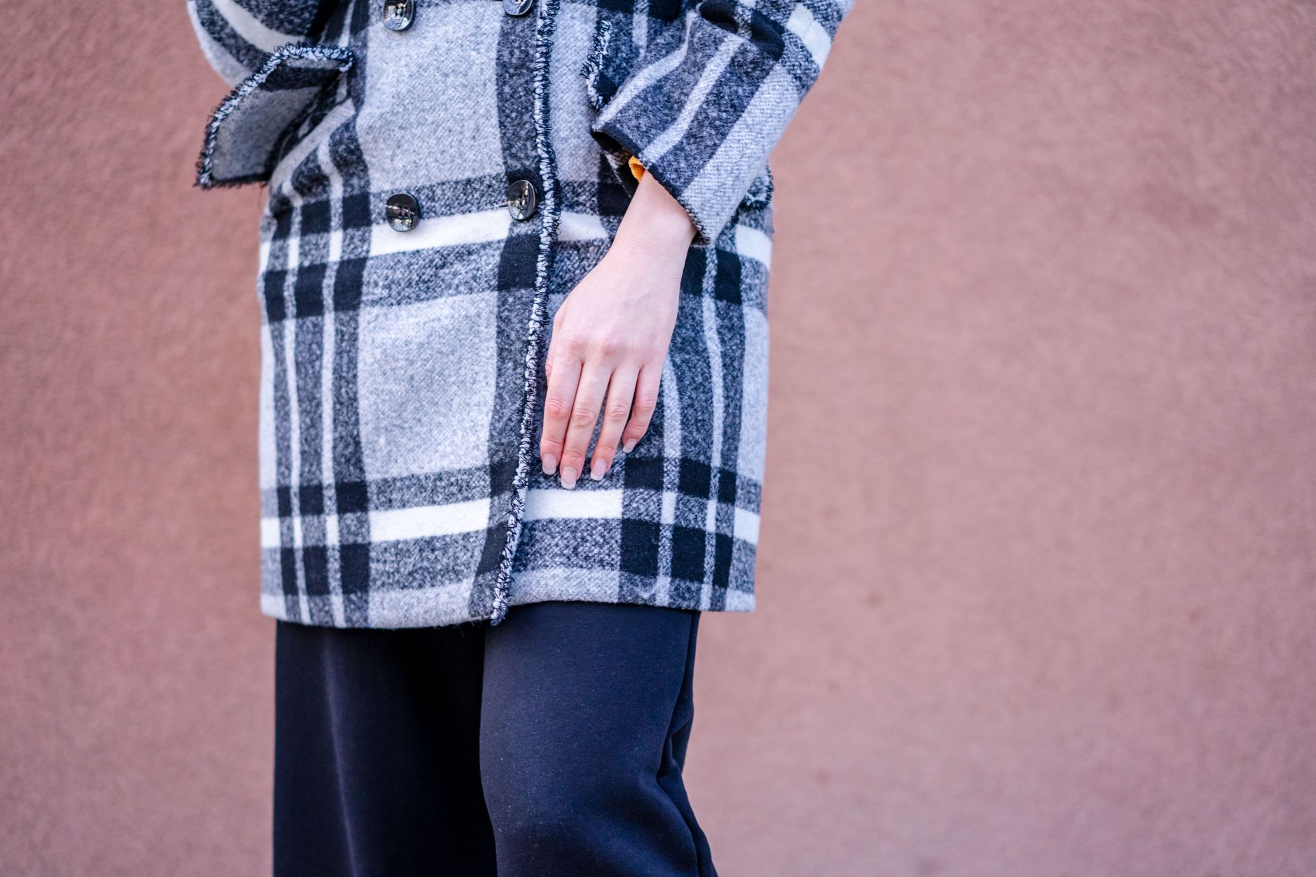 Stylish woman in a plaid wool coat with a gray background, highlighting modern fashion trends.