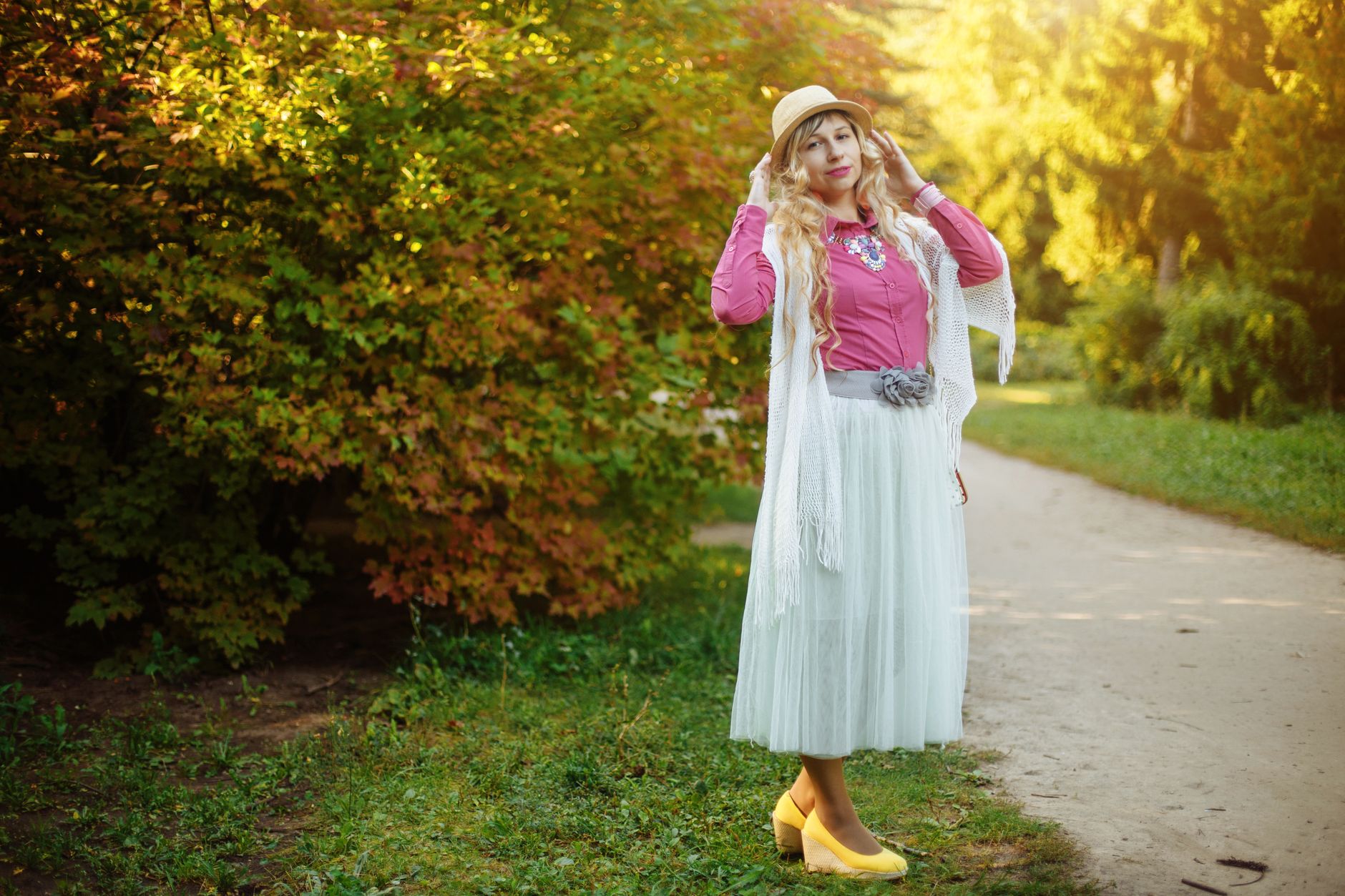 Stylish woman in pink and white posing in autumn park. Fashionable look with hat and accessories.