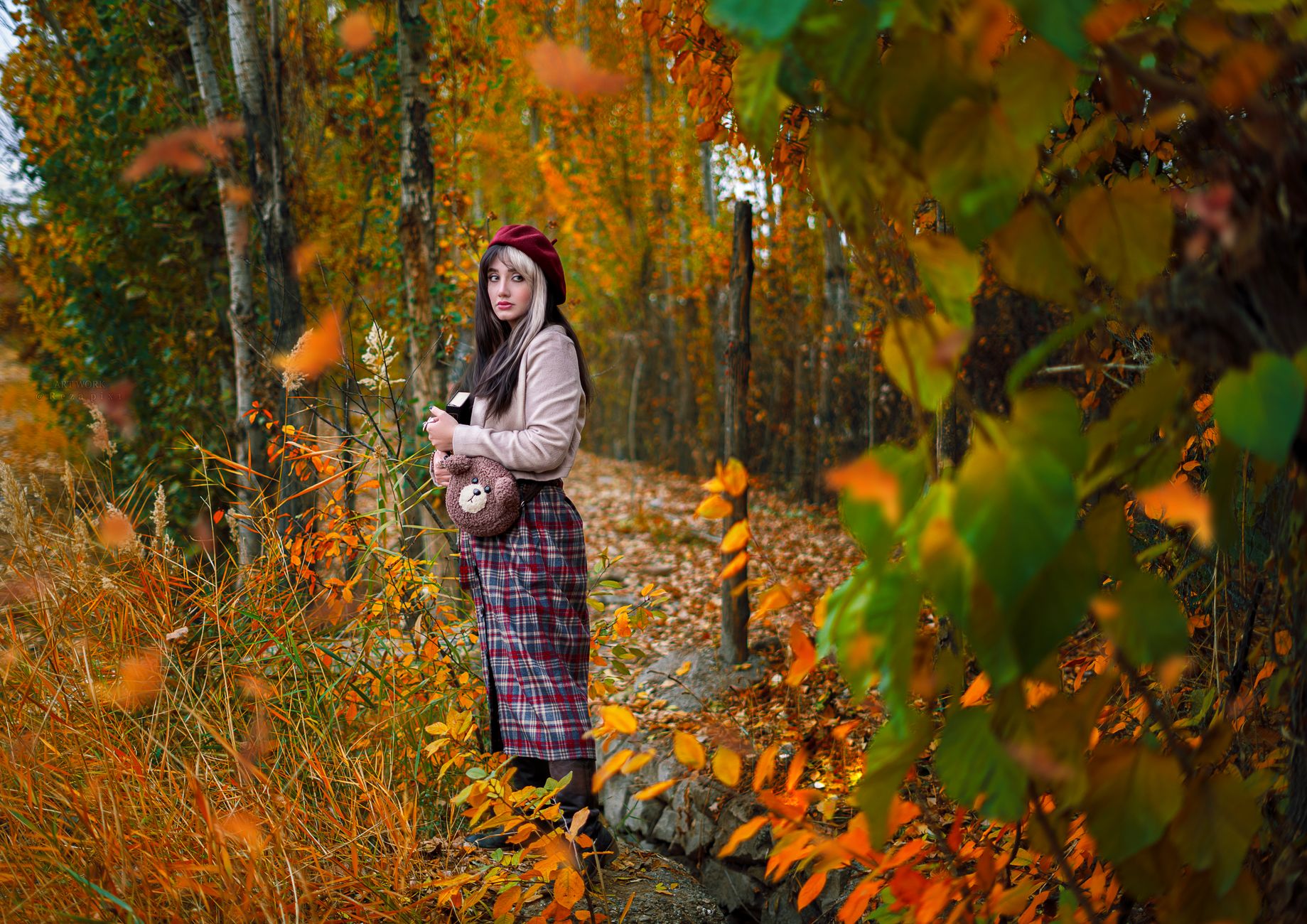 Woman in plaid skirt stands in a vibrant autumn forest, showcasing seasonal fashion.