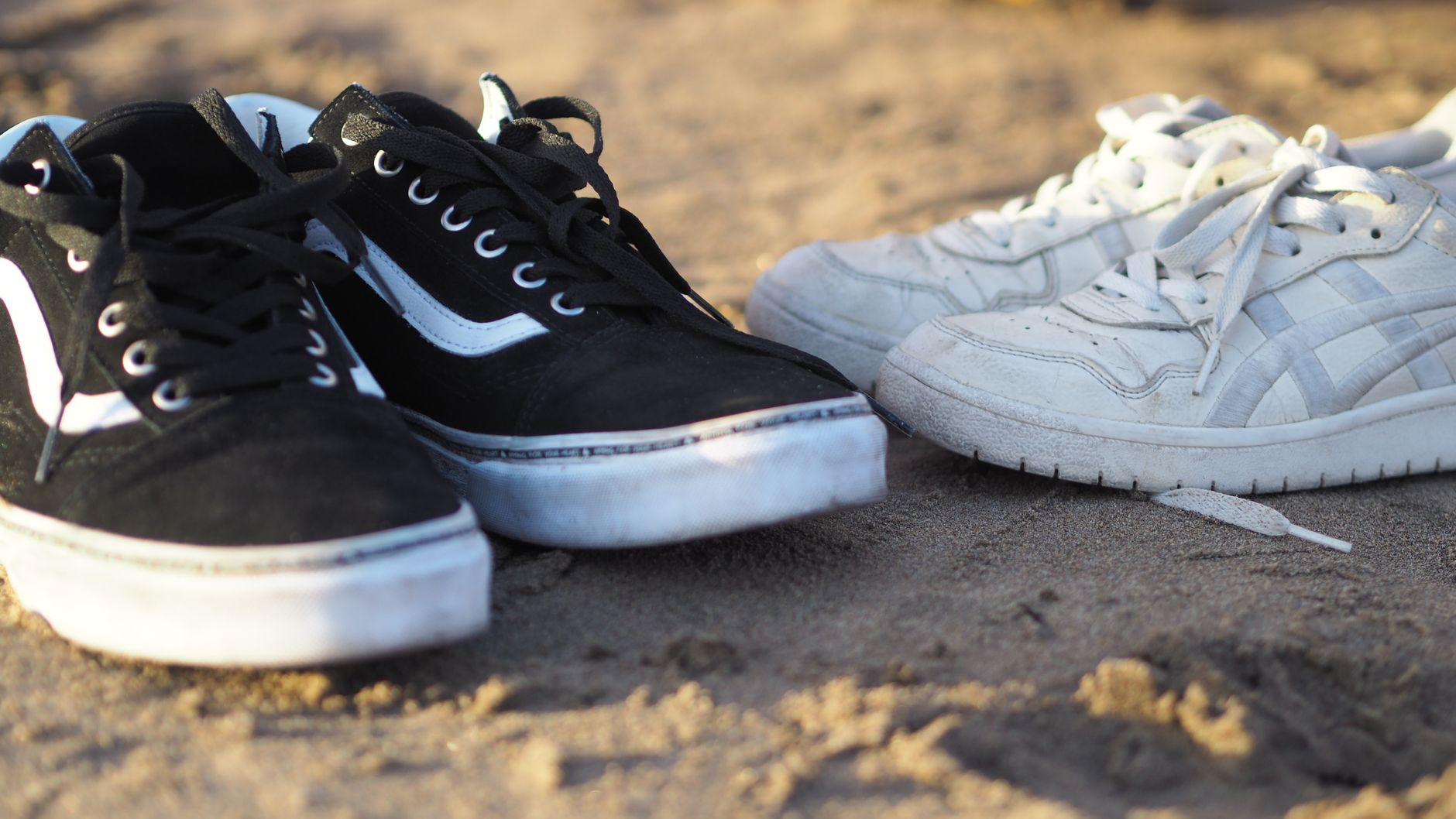 Close-up view of black and white sneakers placed on a sandy beach, perfect for fashion and lifestyle concepts.