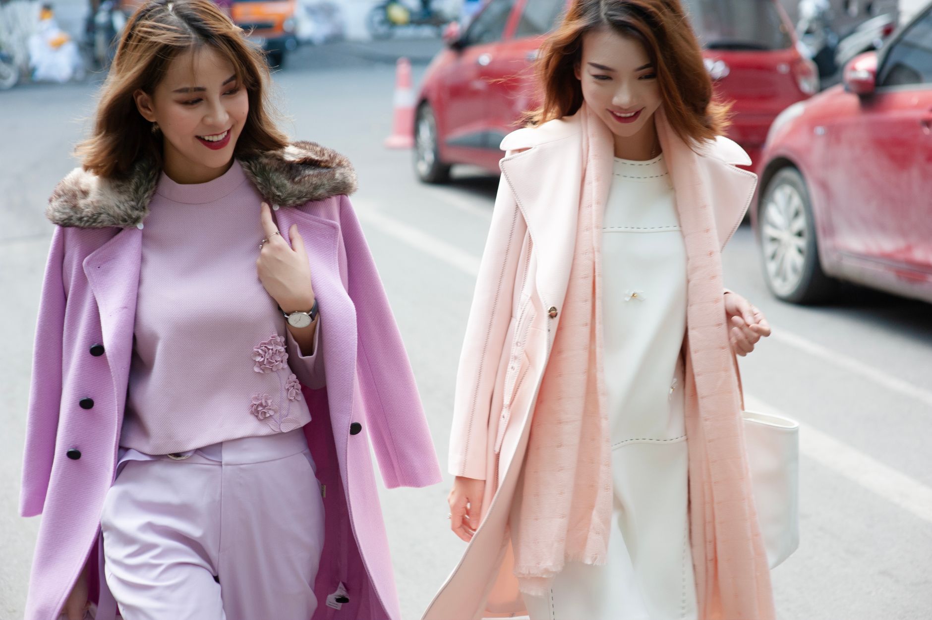 Two stylish women walking in the city wearing pastel coats, exuding confidence and elegance.