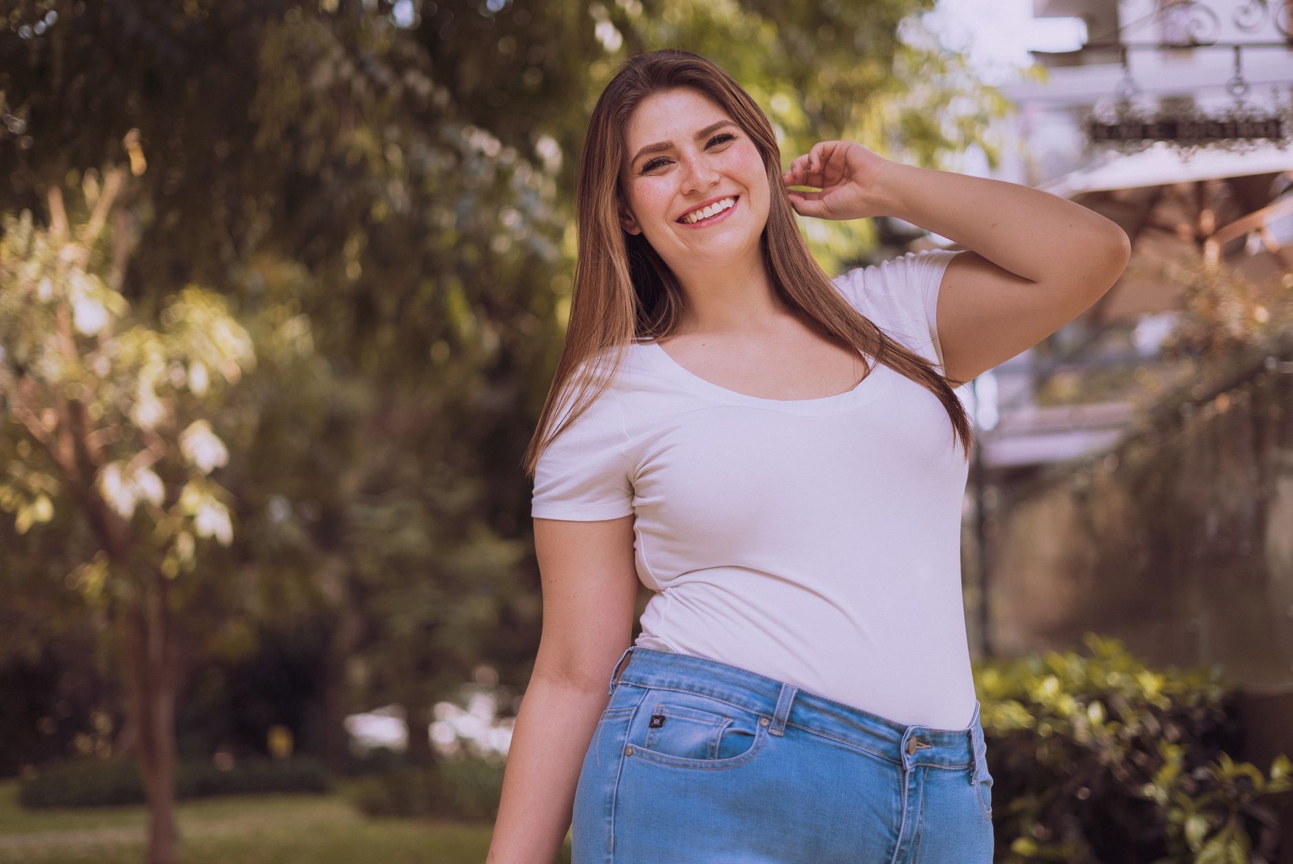 A cheerful plus-size Hispanic woman posing confidently in a serene outdoor setting.