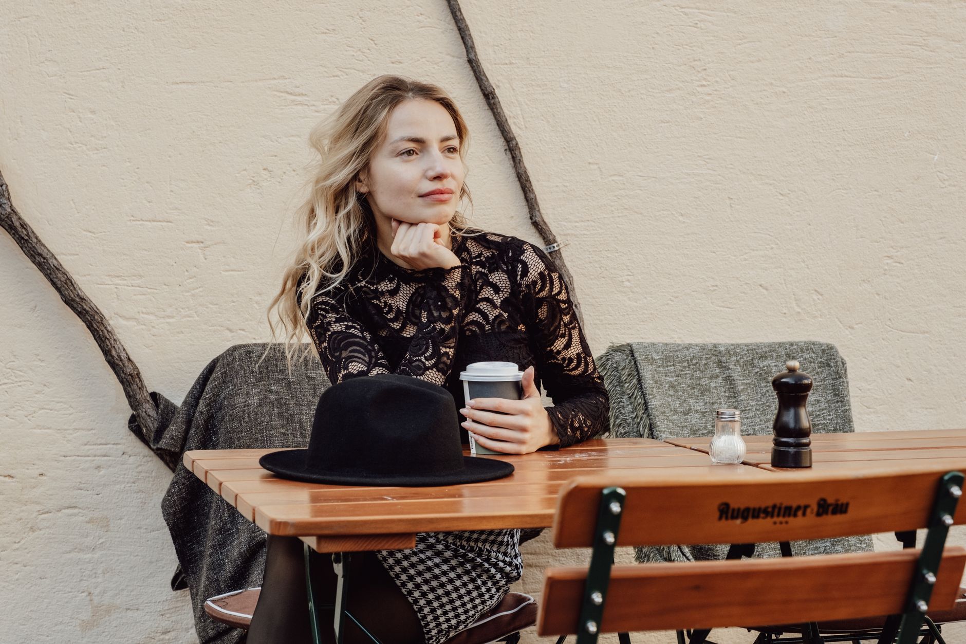 Stylish woman in lace blouse sitting at café table with coffee, embracing relaxation.