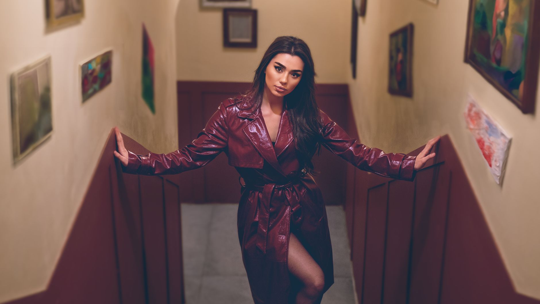 Stylish brunette in a maroon leather coat posing indoors on a staircase.