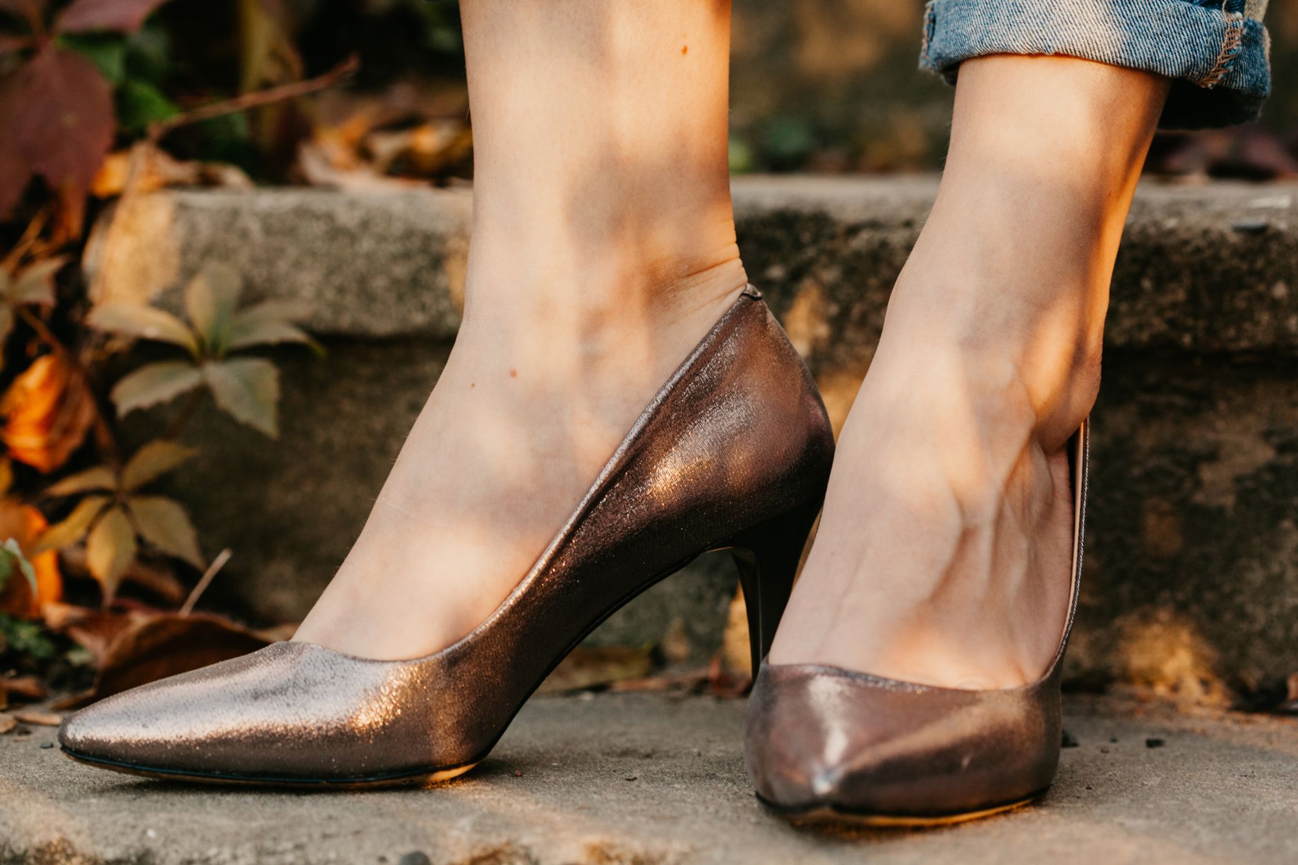 Close-up of female feet in metallic heels, outdoors with autumn leaves.