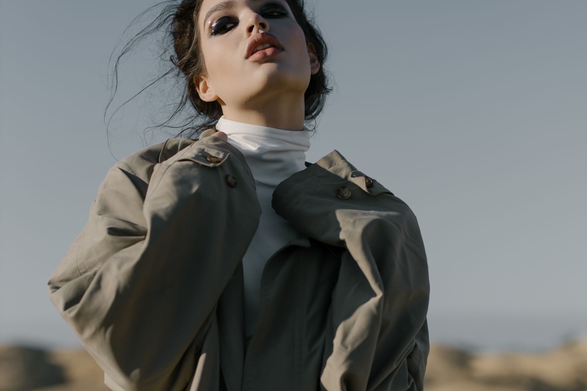 A stylish woman in a trench coat posing outdoors on a sunny day.