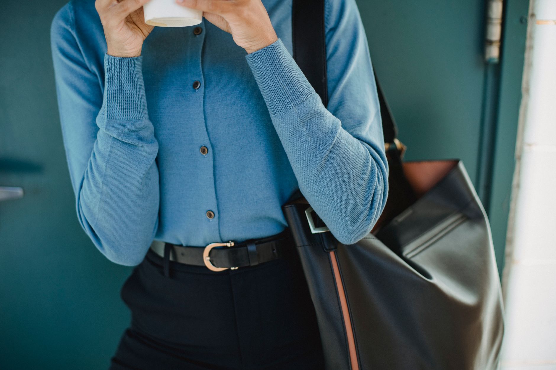 Chic woman in blue cardigan holding a coffee cup, accessorized with a large black tote bag.