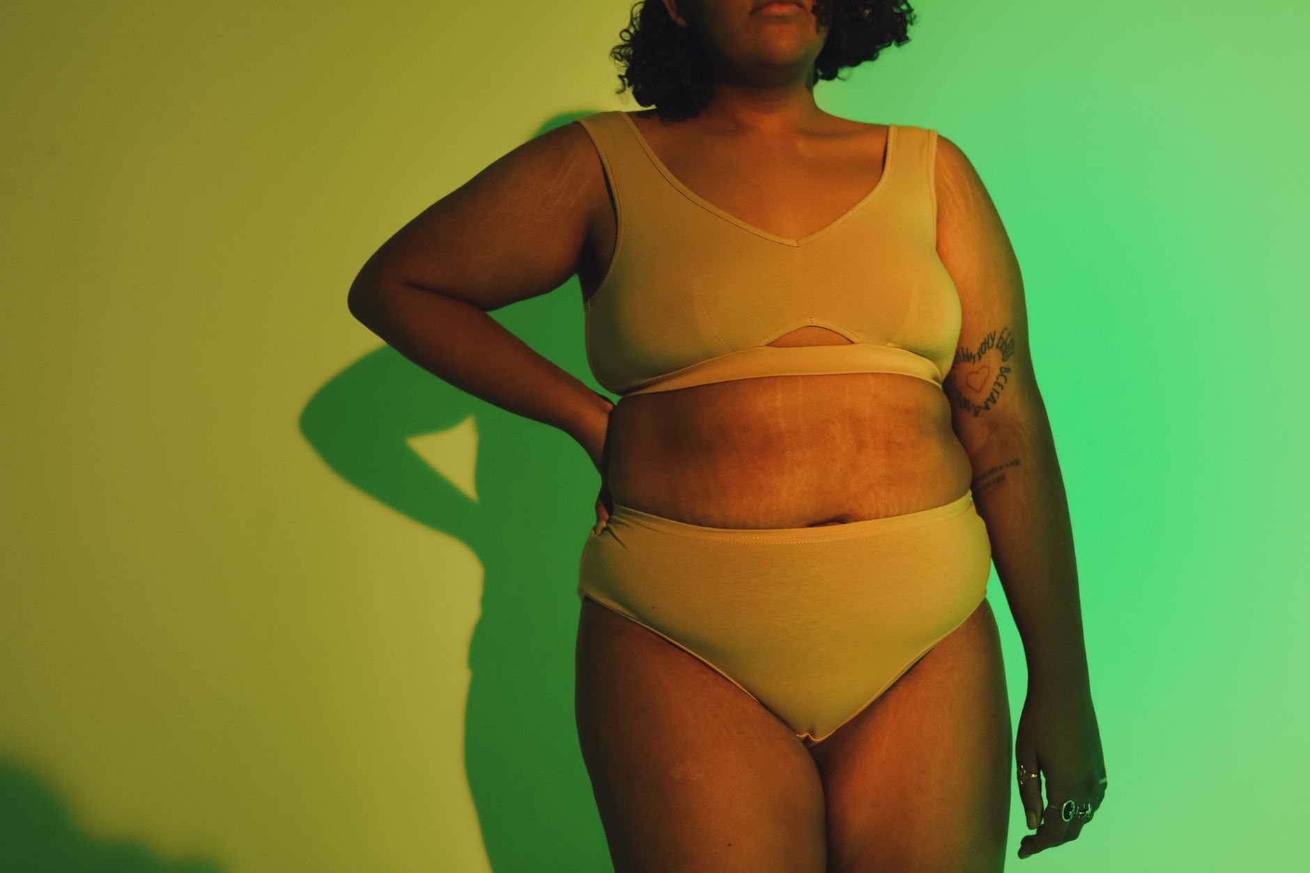 Confident plus-size woman in yellow outfit, standing in studio with creative lighting.