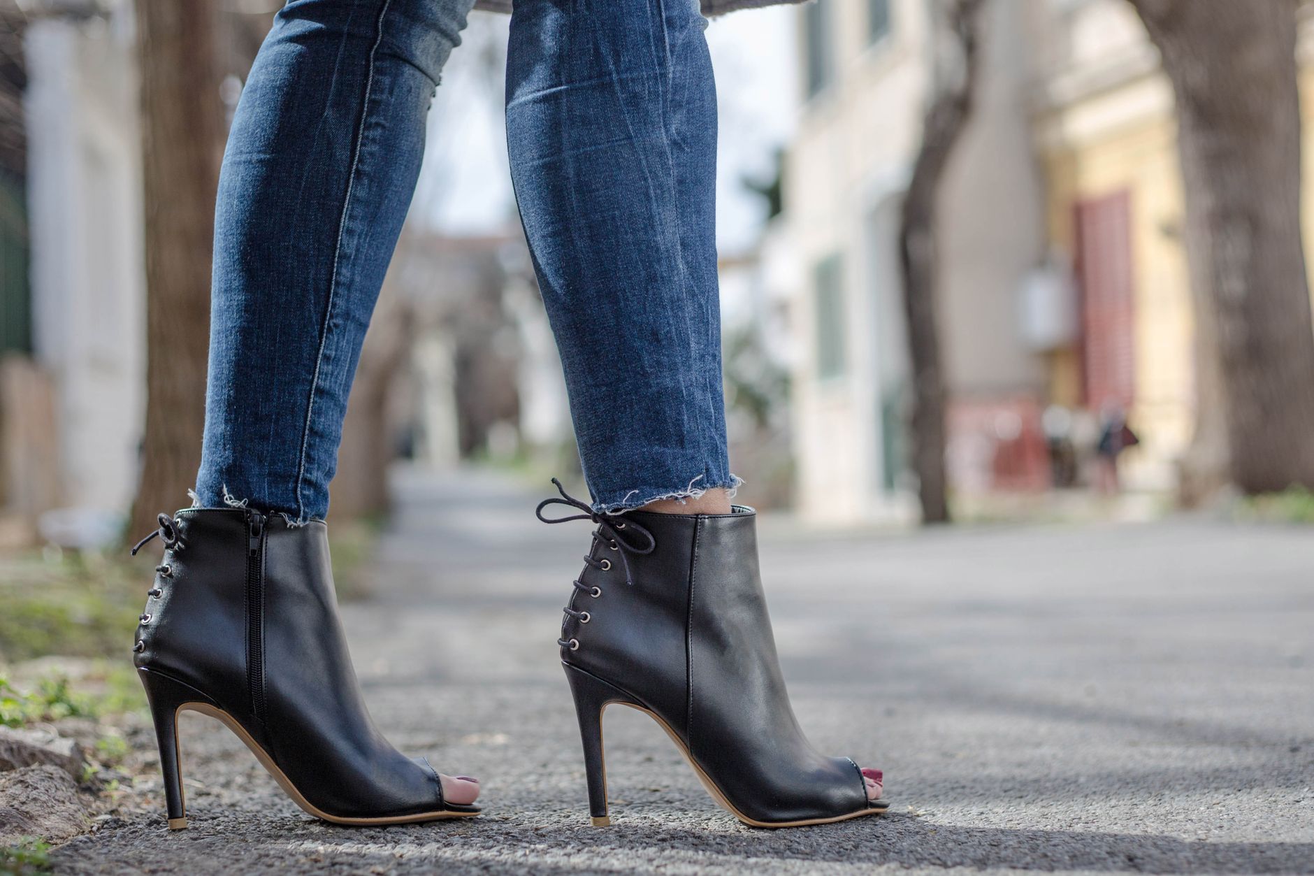 Close-up of woman wearing peep toe stilettos with jeans in an urban environment.