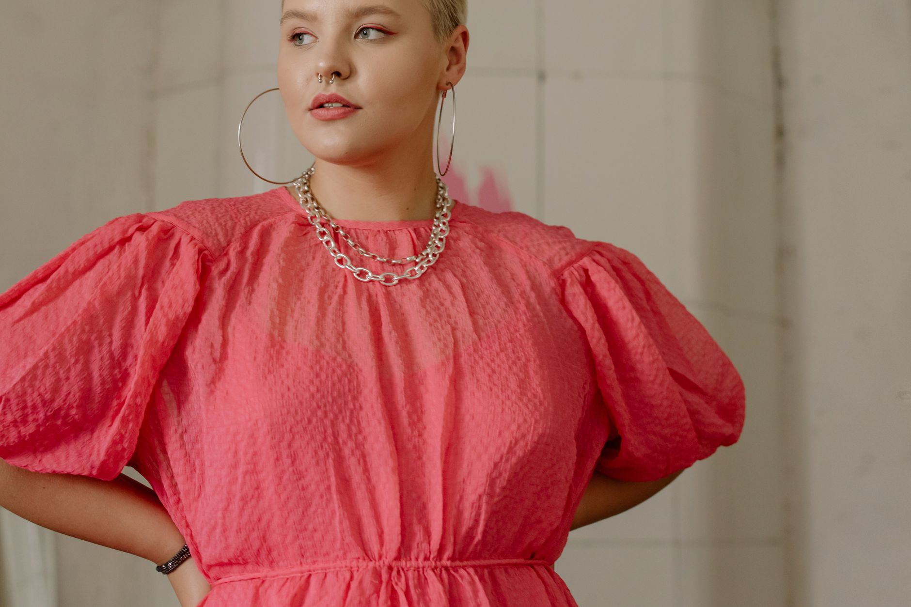 A fashionable woman confidently posing in a vibrant pink dress indoors.
