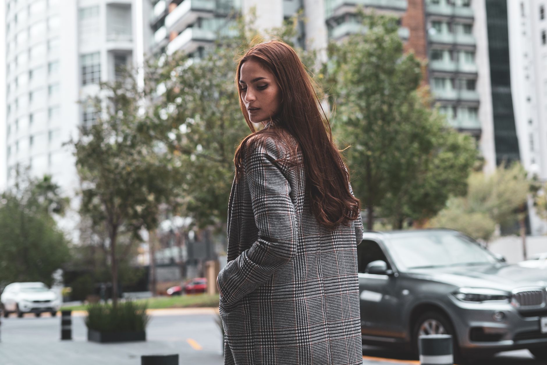 A fashionable woman in a checkered coat stands in a cityscape, embodying urban elegance.