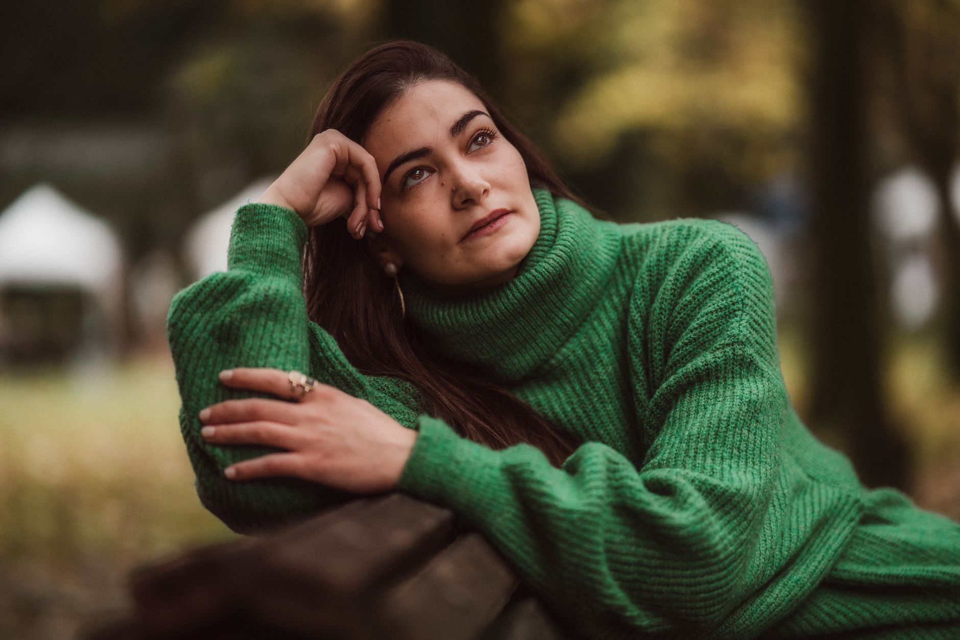 Young woman in green sweater relaxing on a bench in a serene Lisbon park during fall.