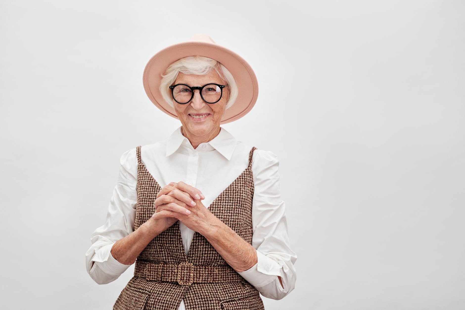 Fashionable senior woman smiling confidently in a stylish outfit with hat and eyeglasses.